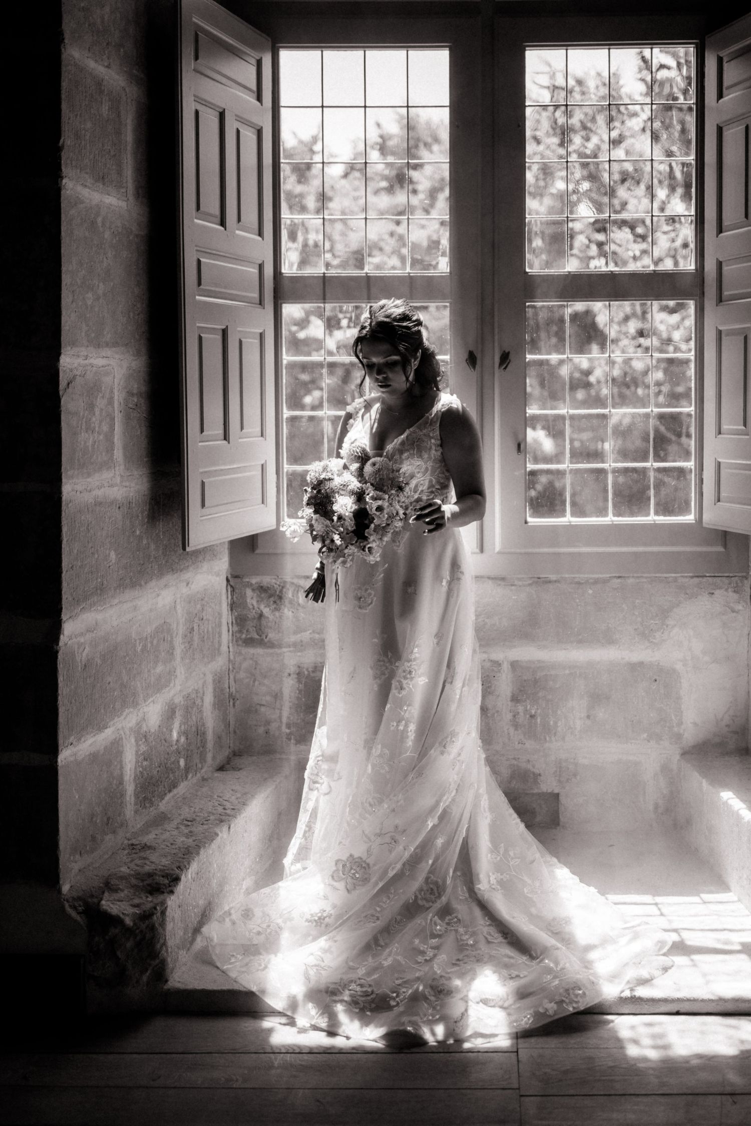 Ethereal black and white photo series showing a bride in flowing lace dress illuminated by dramatic window light.