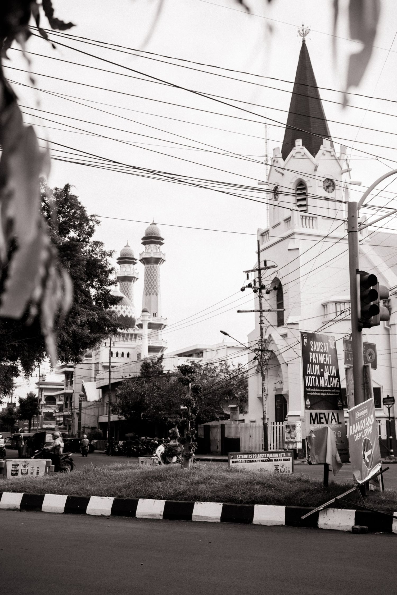 Black and white photo of a church tower and mosque minarets on a busy Indonesian street.