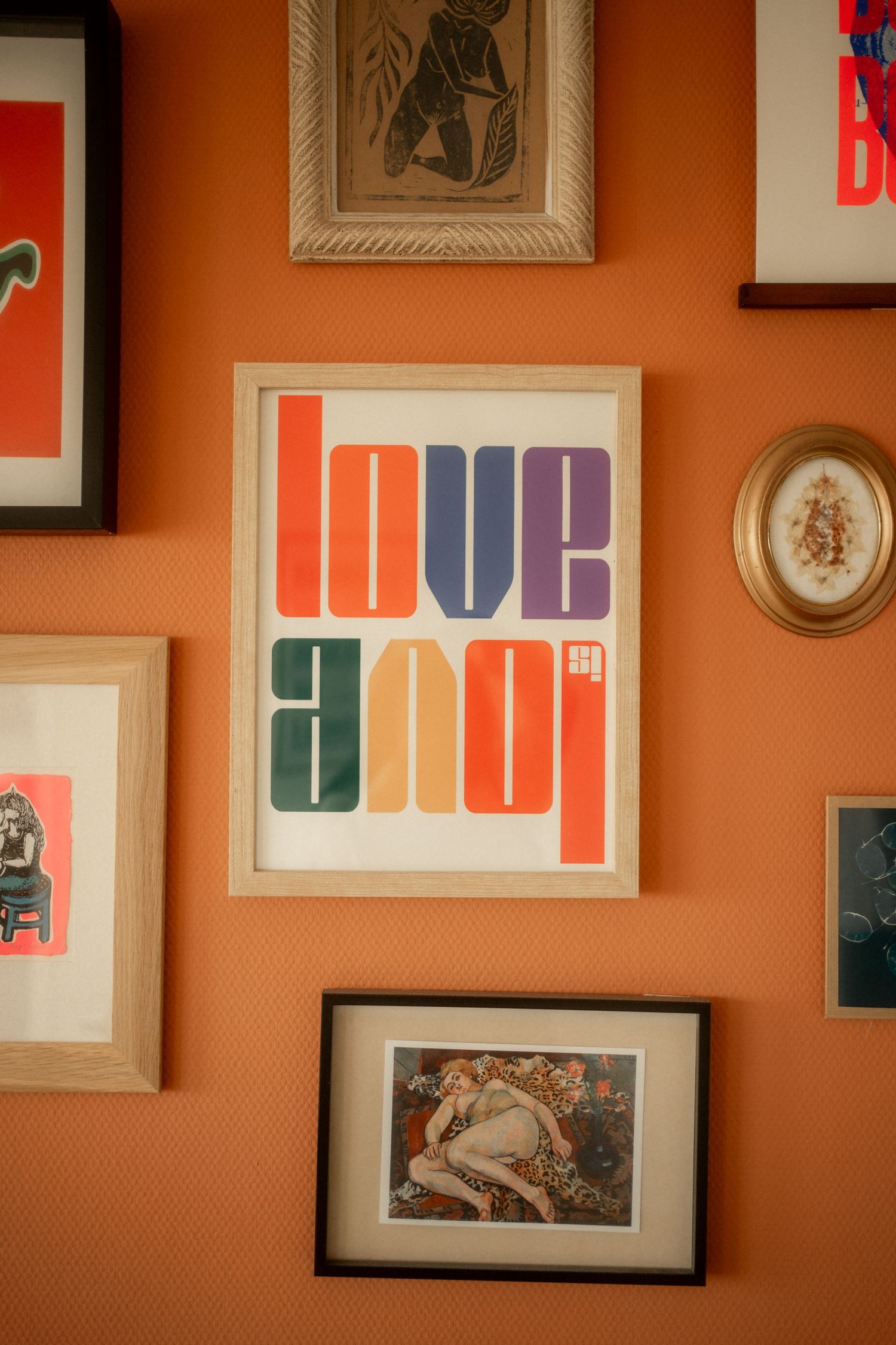 Colorful framed love print on orange wall surrounded by eclectic gallery wall art.