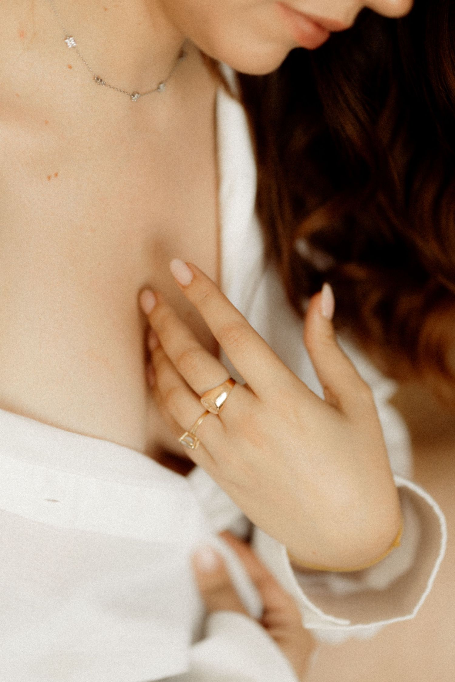 A delicate necklace and engagement ring are showcased on a person wearing white.