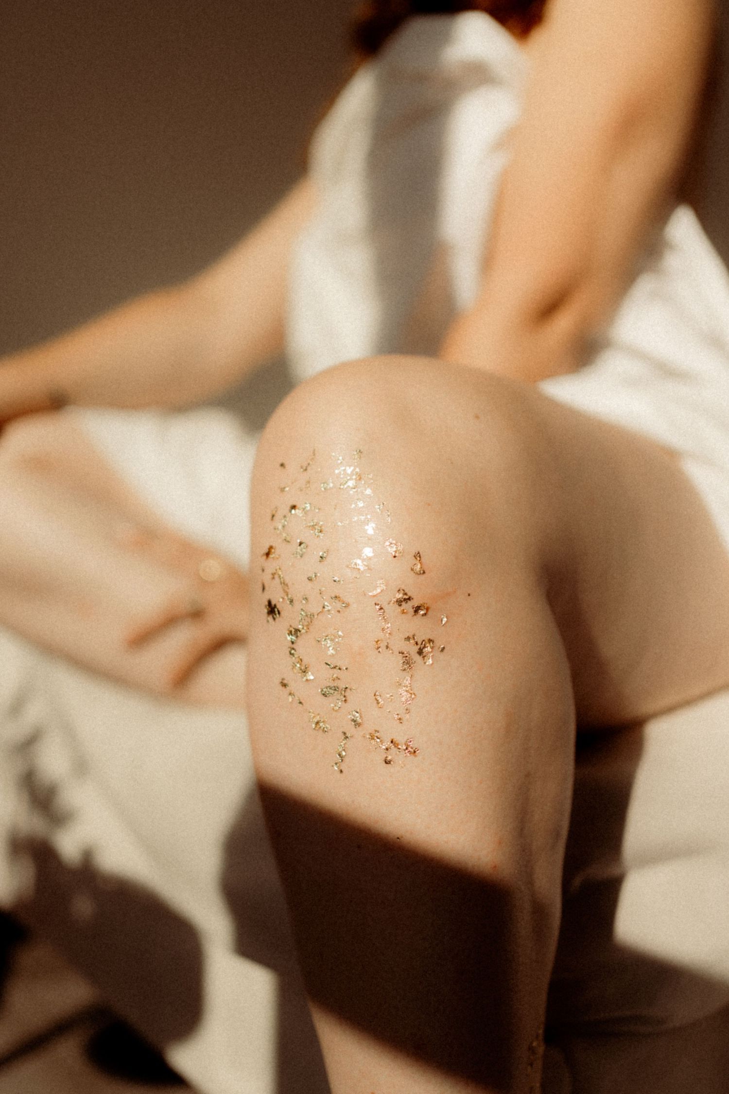 Glittery gold sparkles shimmer on skin against white fabric in soft lighting.