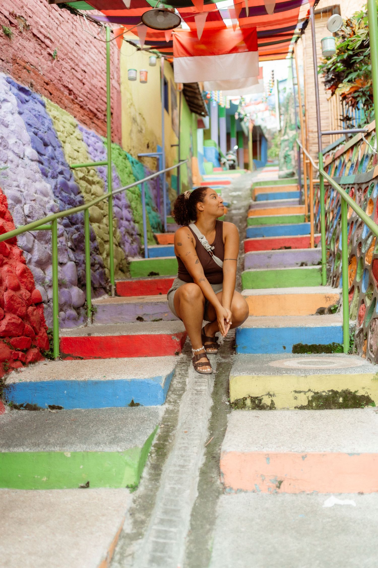 Woman sitting on colorful painted steps in a vibrant alleyway with rainbow-colored walls and stairs.