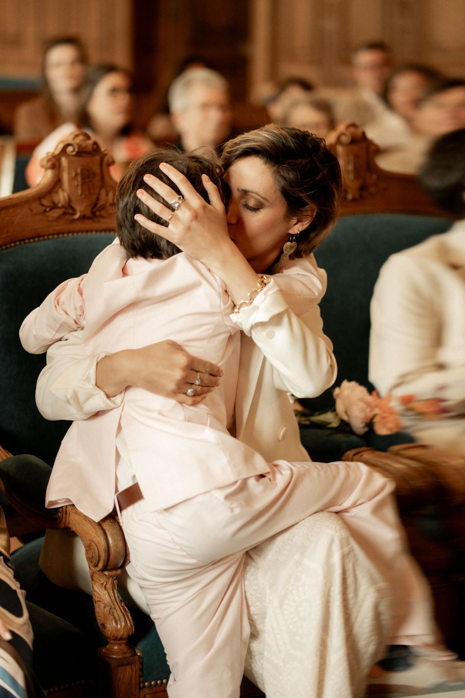 Two brides in elegant suits share an emotional embrace during their wedding ceremony.