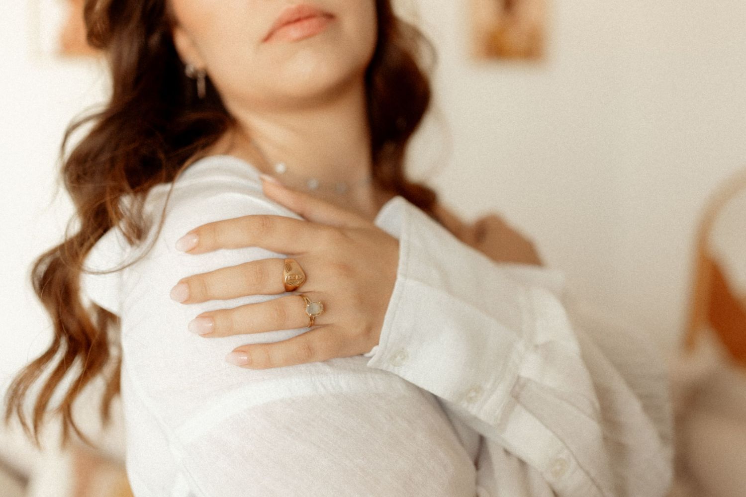 Woman with long brown wavy hair wearing a white top poses against a neutral background.