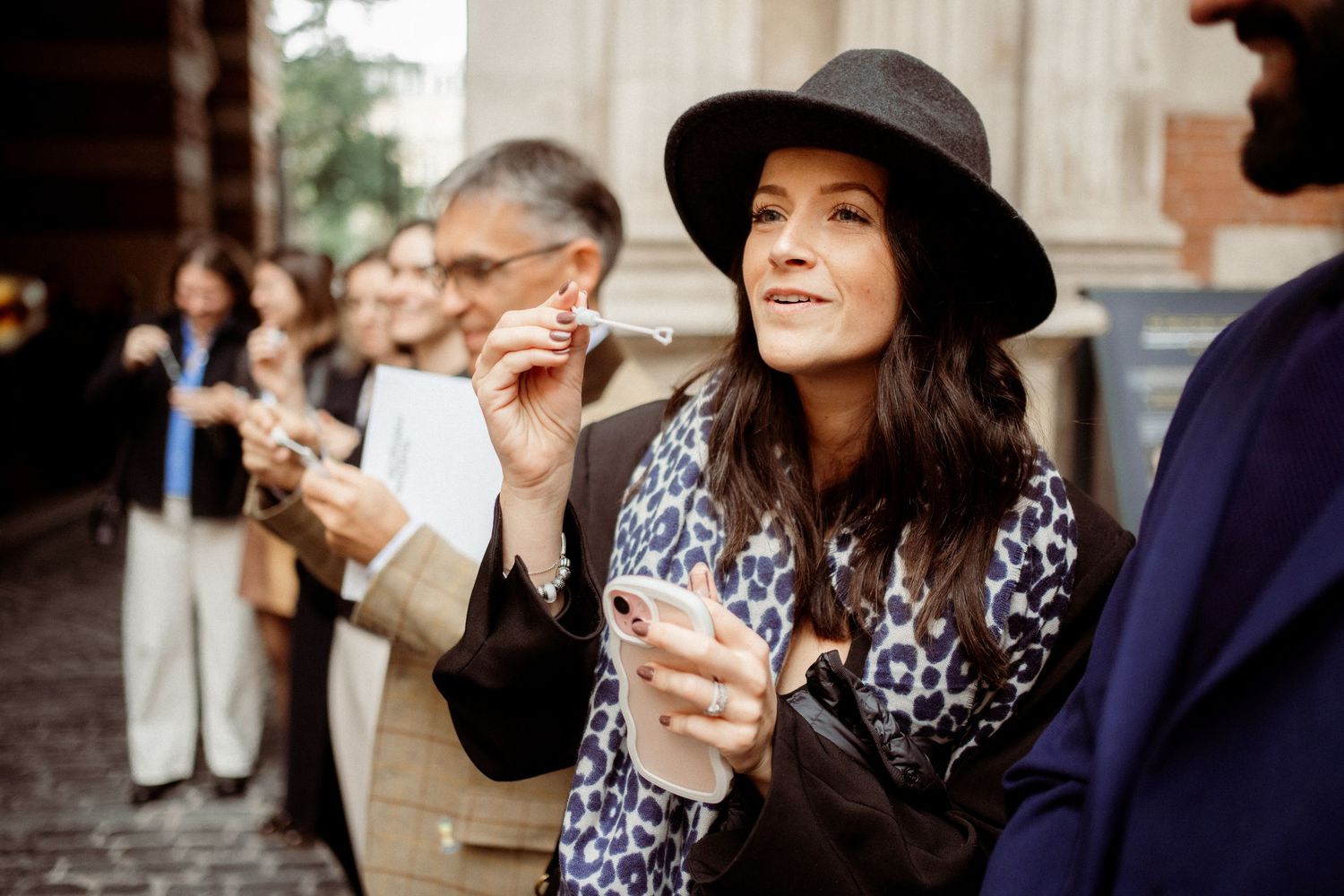 Stylish woman in black hat and leopard print jacket holding sparkler at outdoor wedding celebration.
