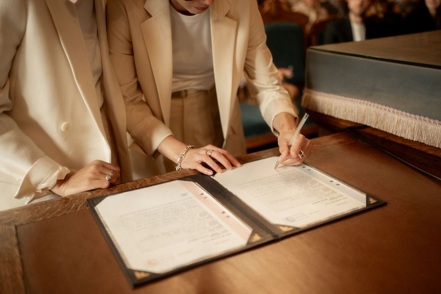 Bride signing wedding registry document in an open leather binder on a wooden table during a marriage ceremony.