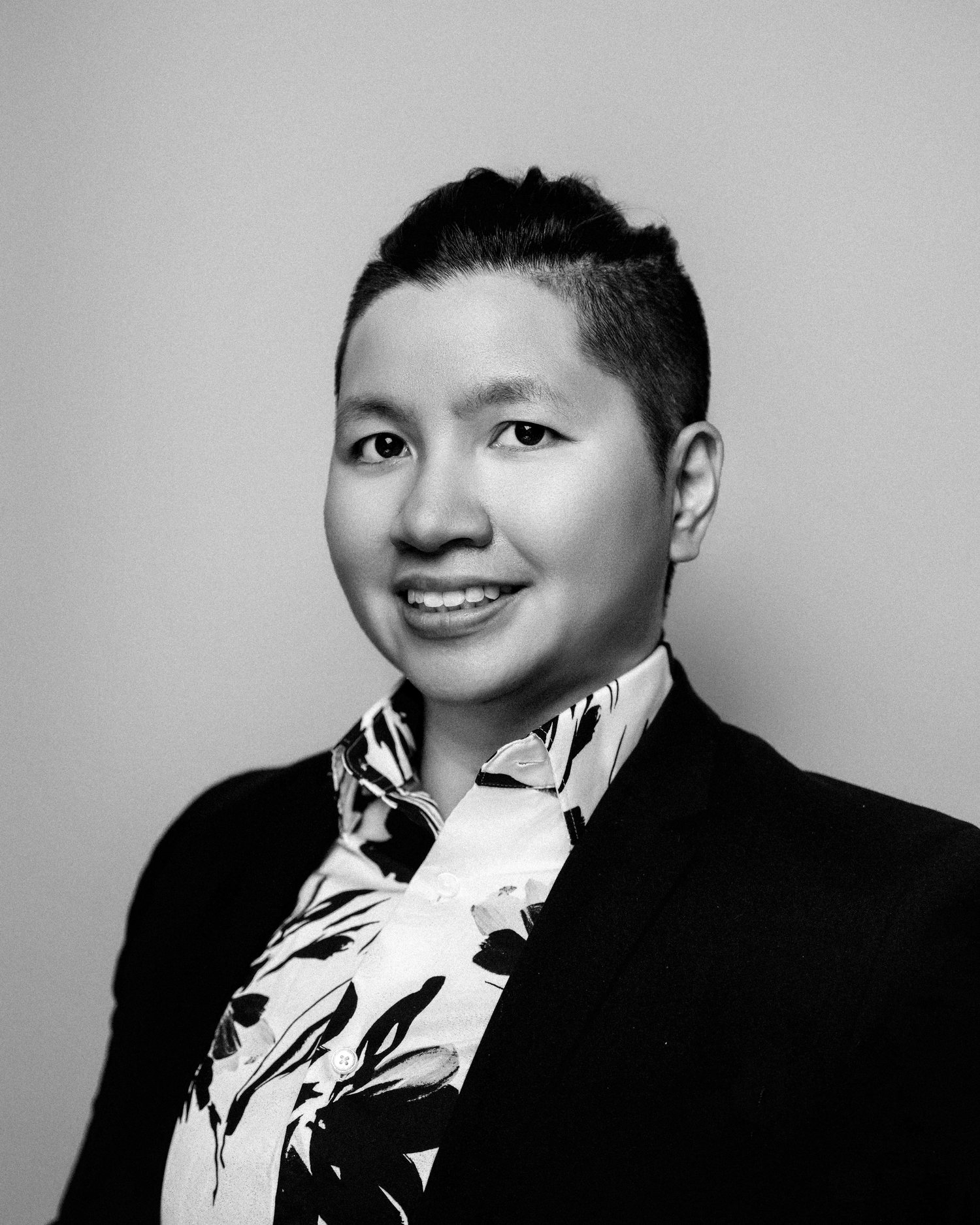 A black and white professional headshot of someone wearing a black sweater and patterned scarf.