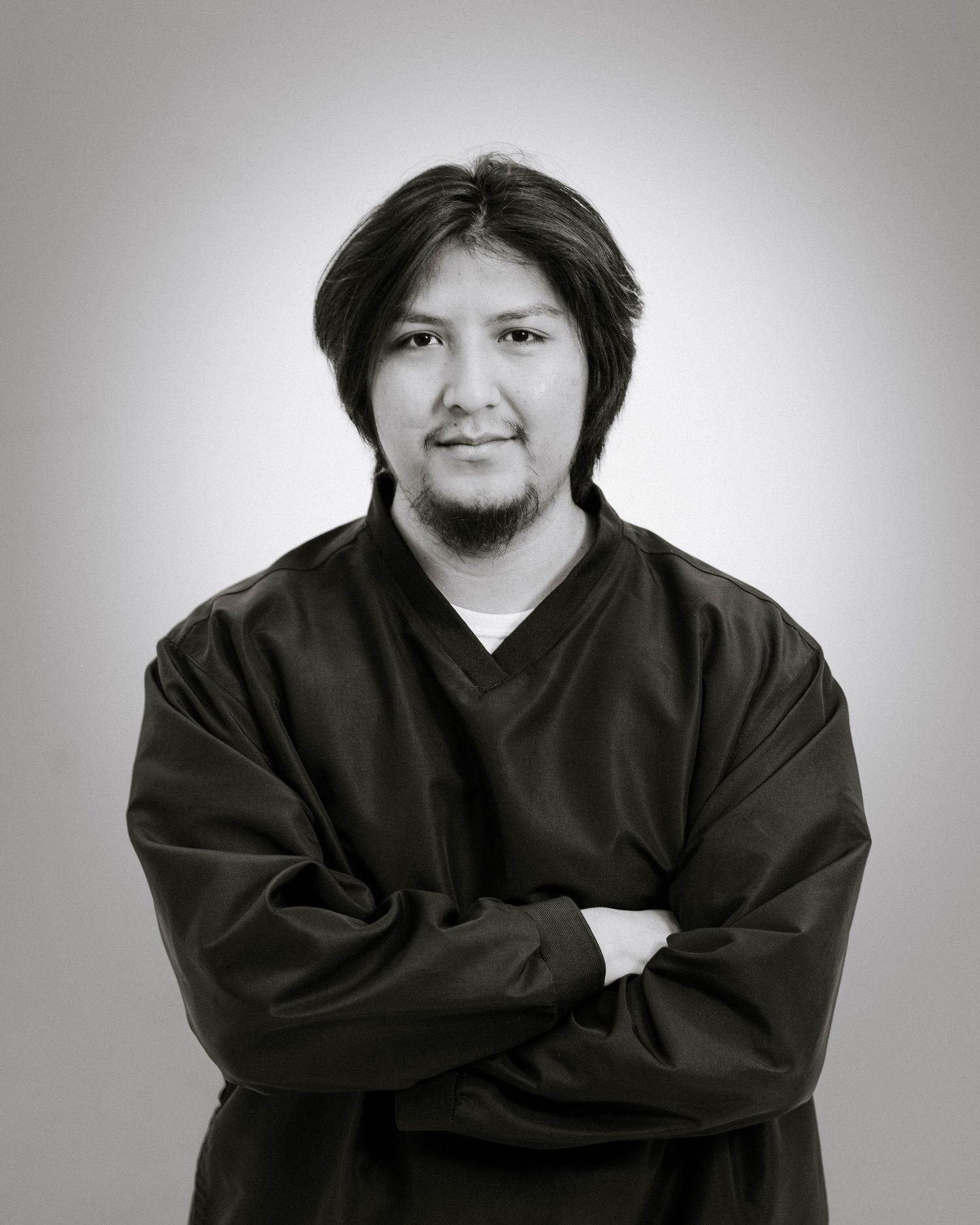 Black and white studio portrait of a person in dark v-neck top with arms crossed against a gradient background.