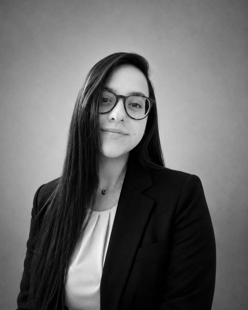 Black and white professional headshot of a young woman with long hair and glasses wearing a blazer.