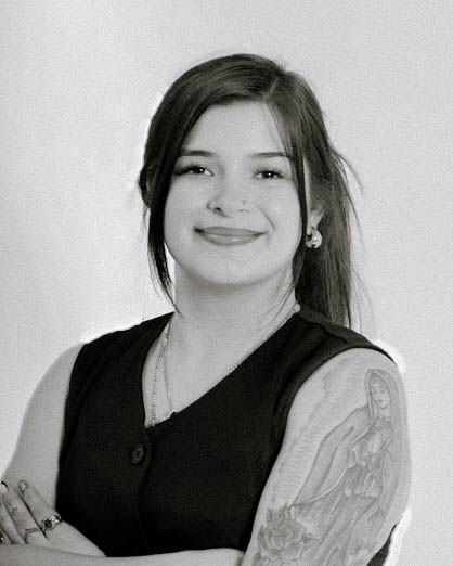 A black and white portrait of a woman in a sleeveless top smiling at the camera, showing a visible arm tattoo.