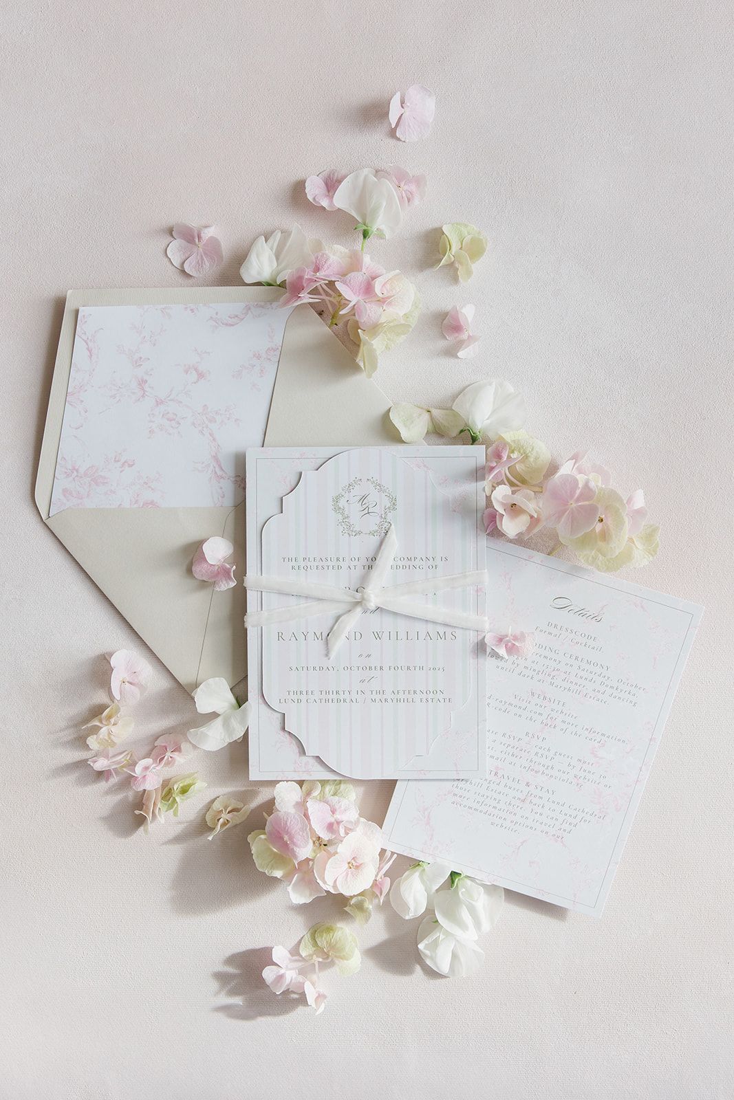 Elegant white wedding invitation cards with delicate pink cherry blossoms scattered on light beige background.