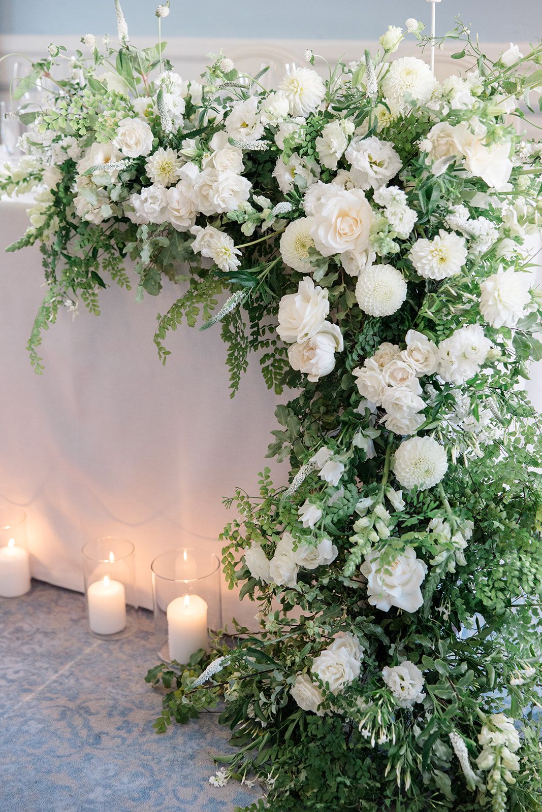 Elegant white roses and greenery floral arrangement with glowing candles creating romantic wedding decor.