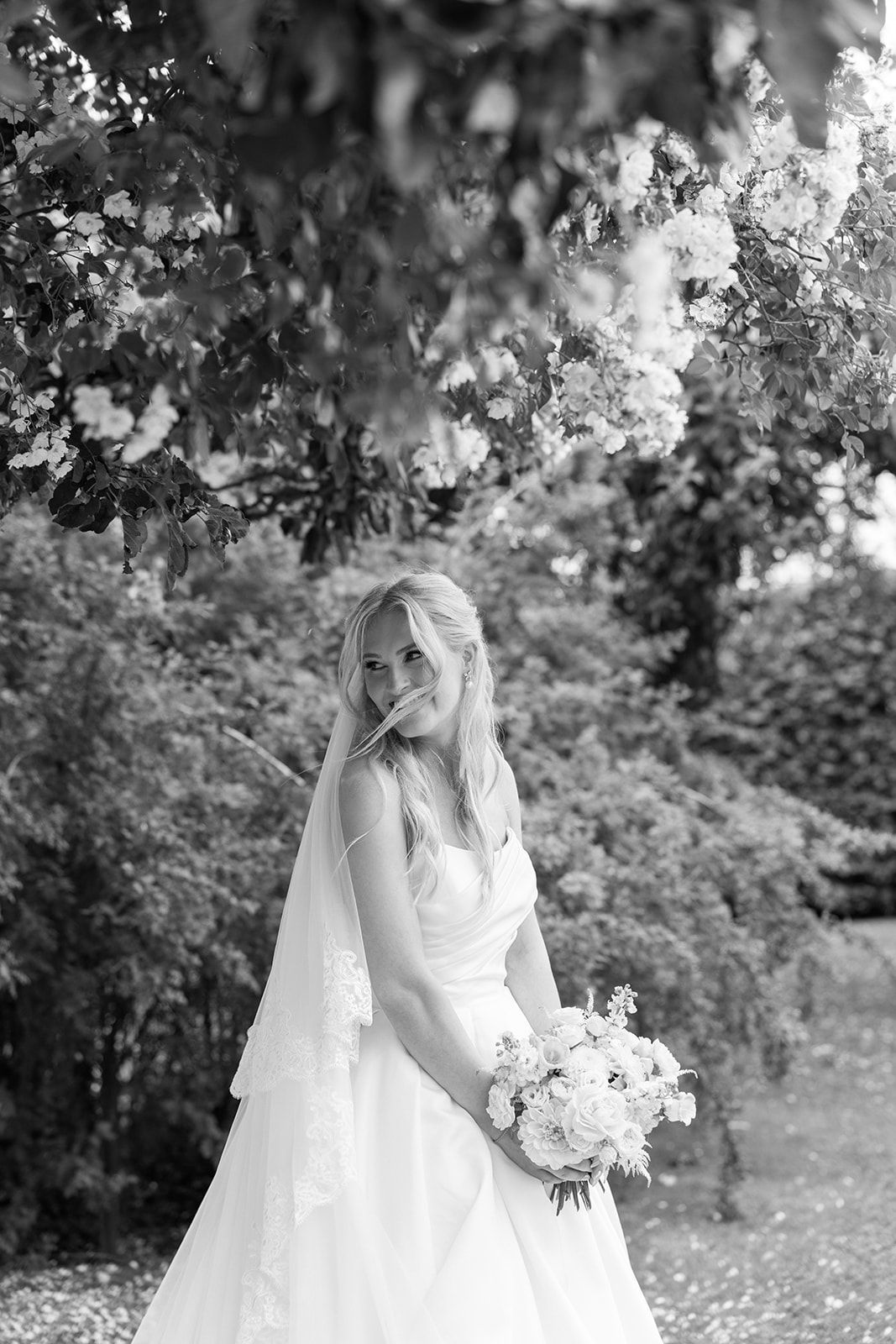 A bride in a flowing white wedding gown holds a bouquet of white flowers in a lush garden setting.