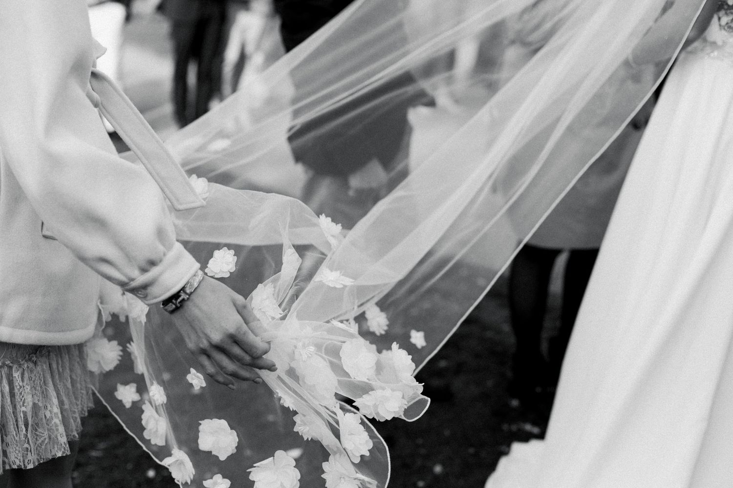 Delicate hands adjust a wedding veil with floral details in an intimate black and white moment.