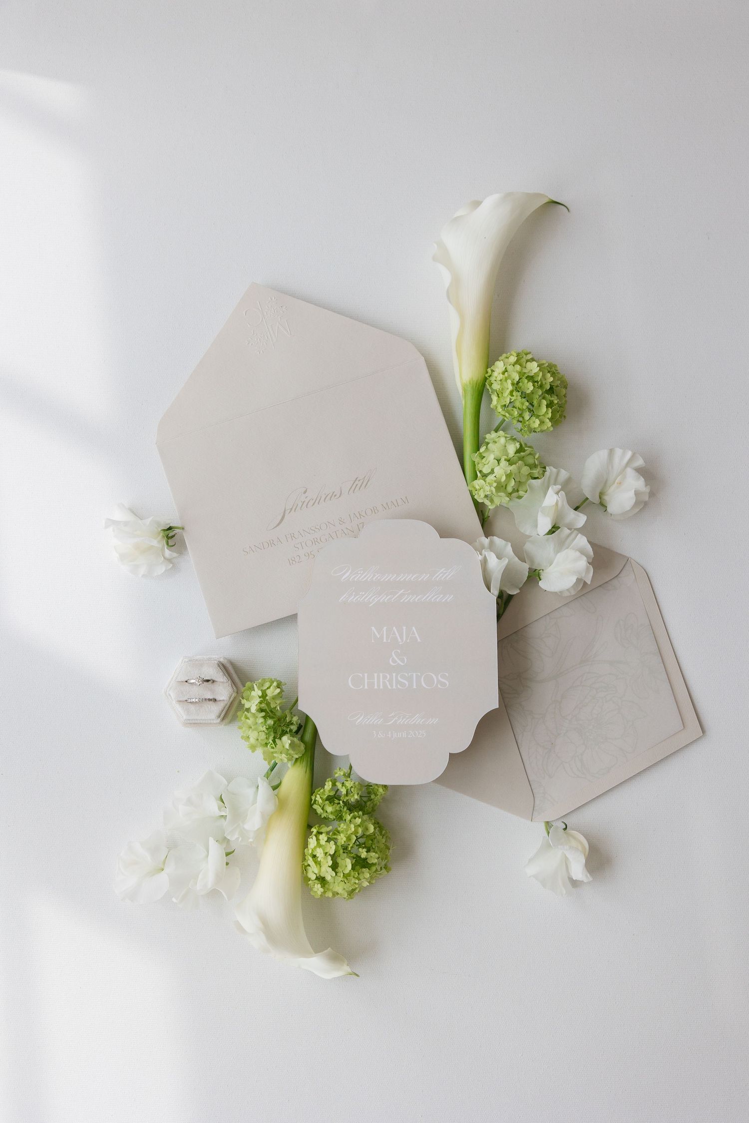 Wedding invitation surrounded by elegant white calla lilies, green hydrangeas and delicate floral accents on light background.