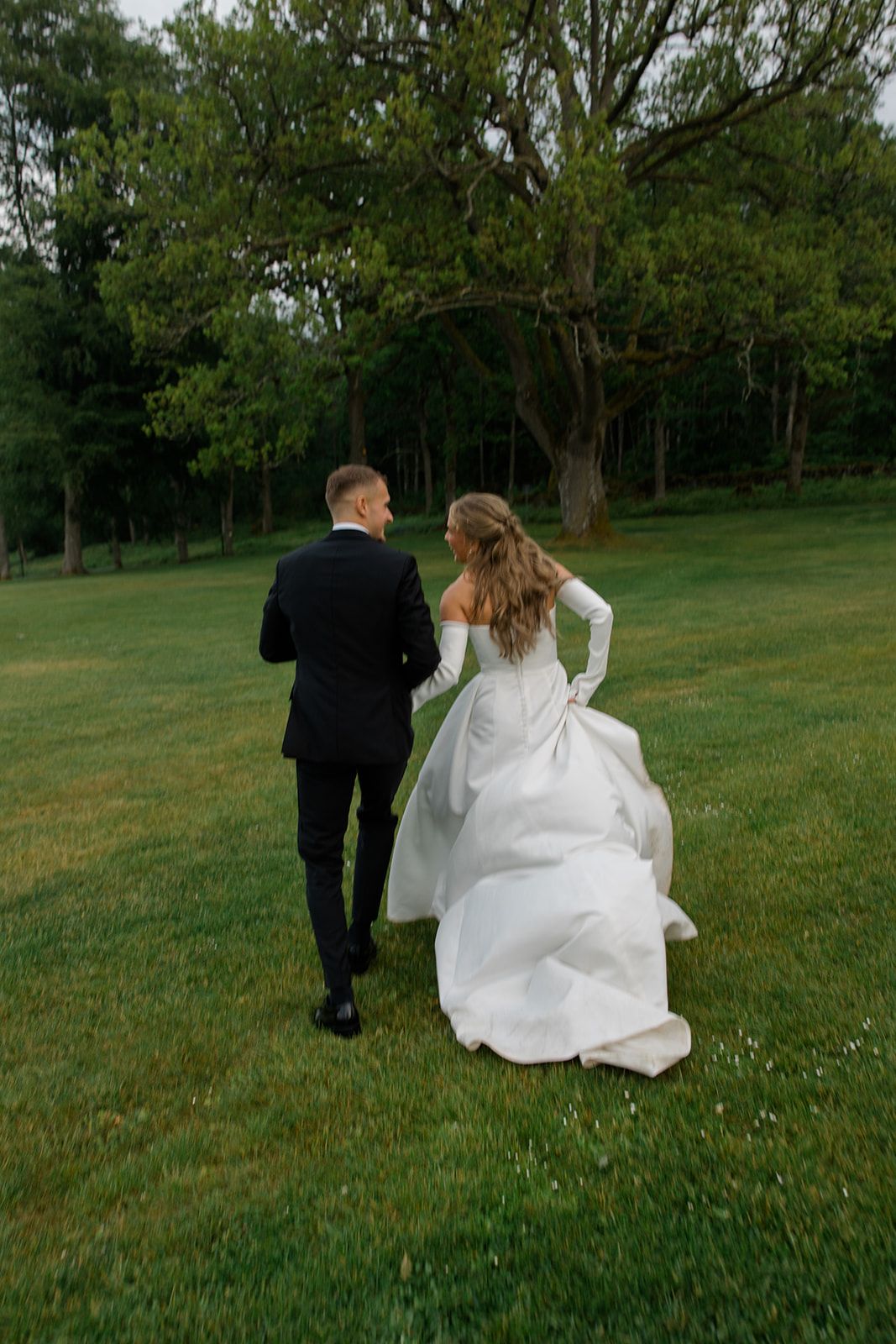A couple walking together through a green field on an overcast day.