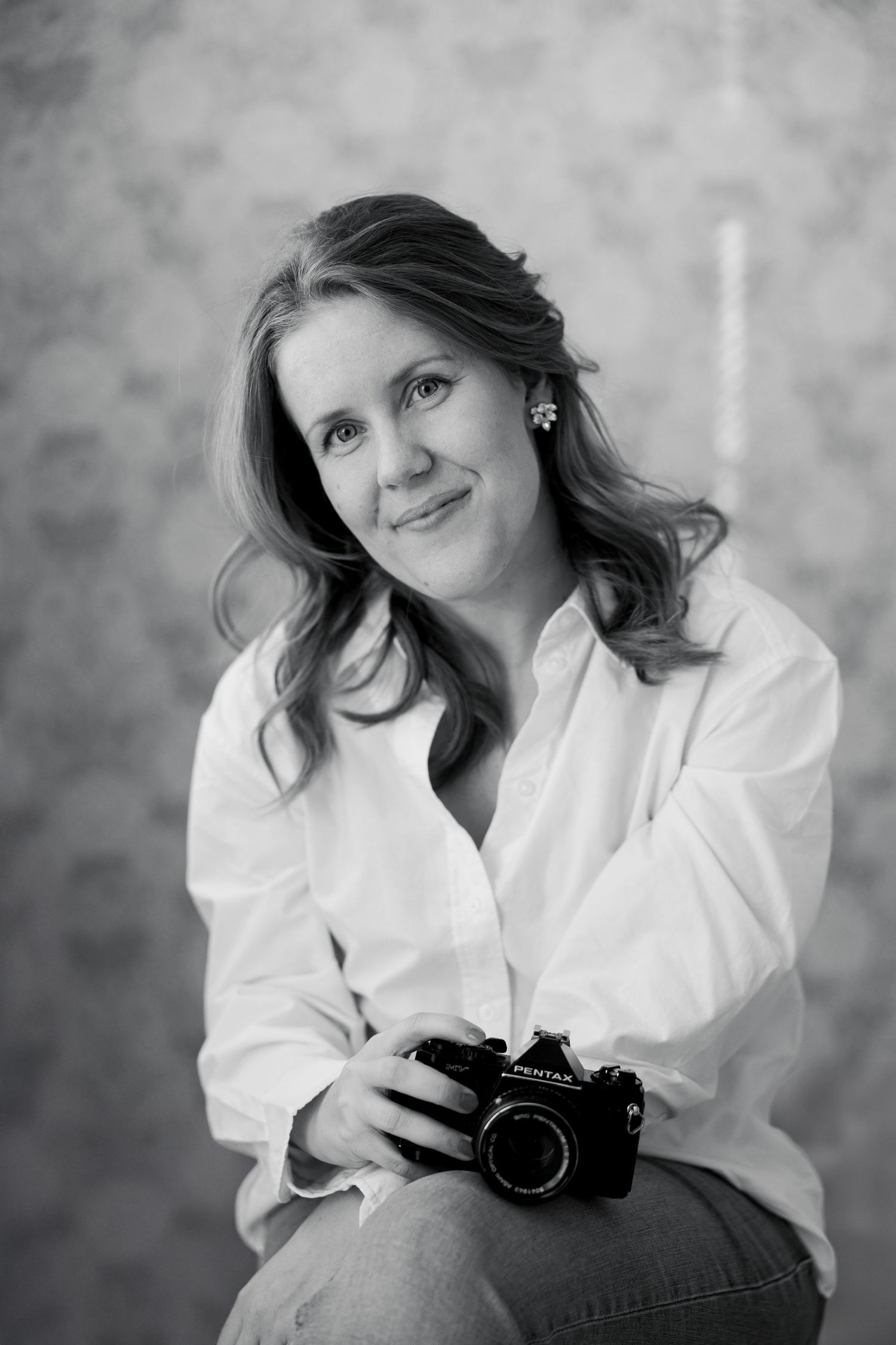 Black and white portrait of a photographer in a white shirt holding a vintage camera and smiling at the camera.