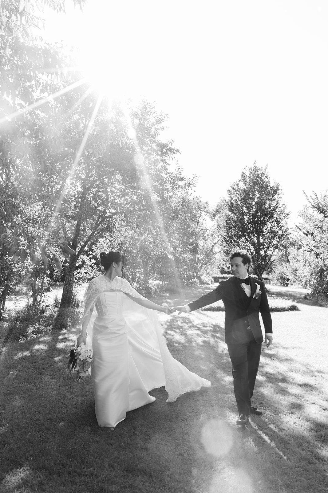 A couple in wedding attire walks together on a sunlit hillside in a series of romantic black and white photographs.