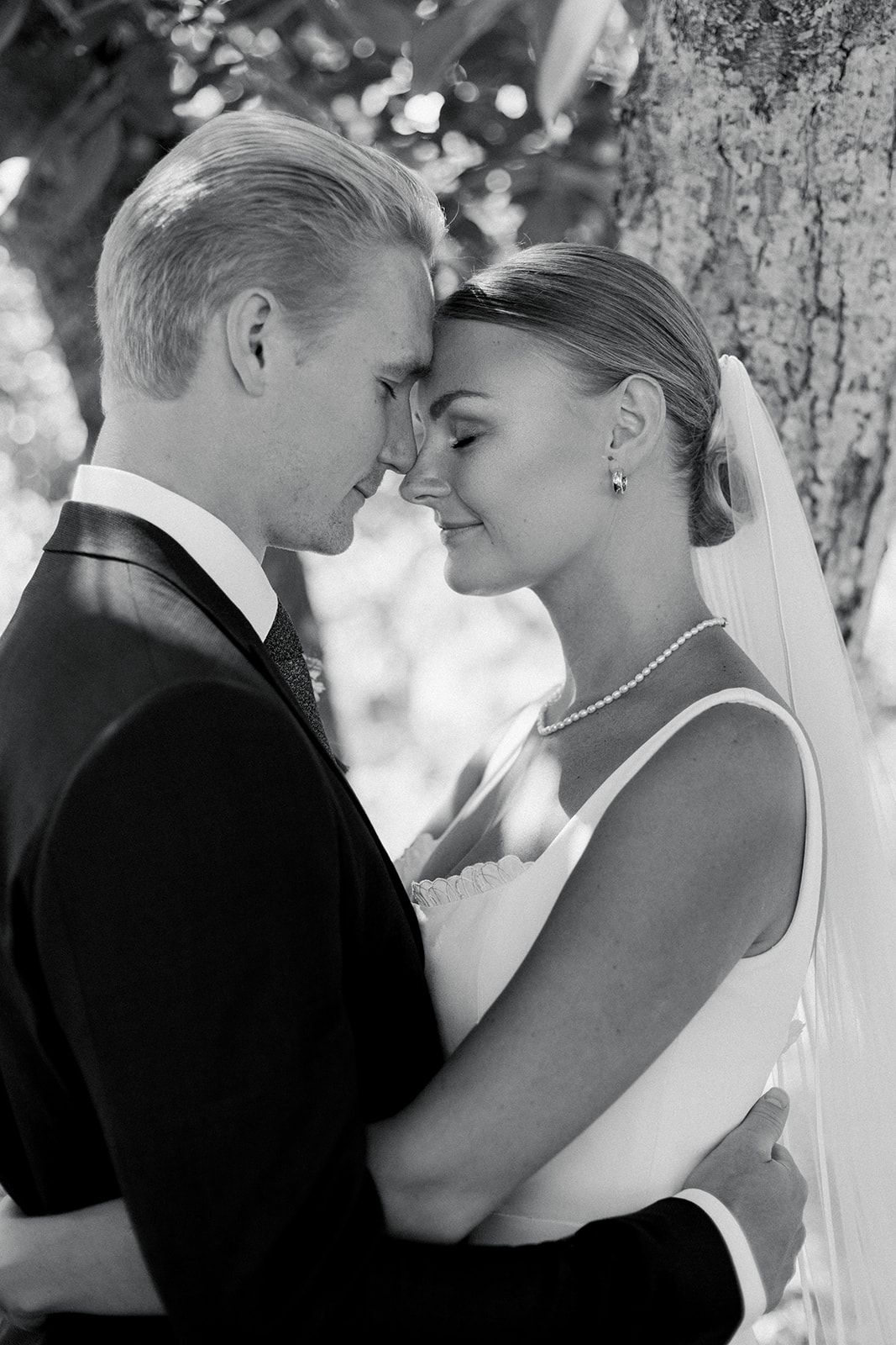 A romantic black and white wedding photo series showing tender moments between a bride and groom under trees.