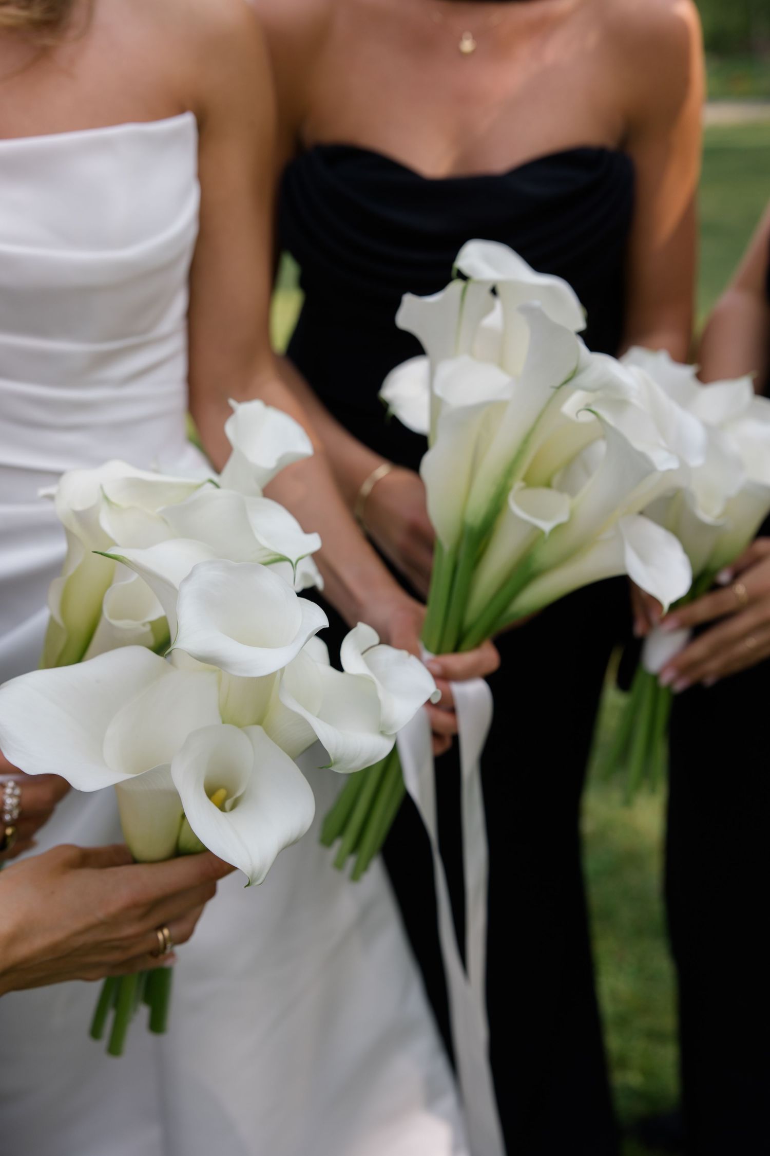 Bridesmaids in black and white dresses hold elegant white calla lily bouquets with silk ribbons.