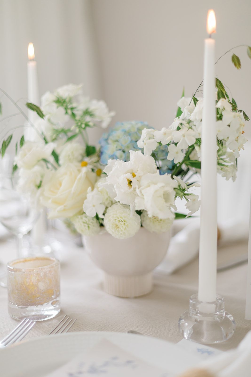 Elegant white table setting with delicate floral arrangements in small vases and glowing taper candles create a romantic ambiance.