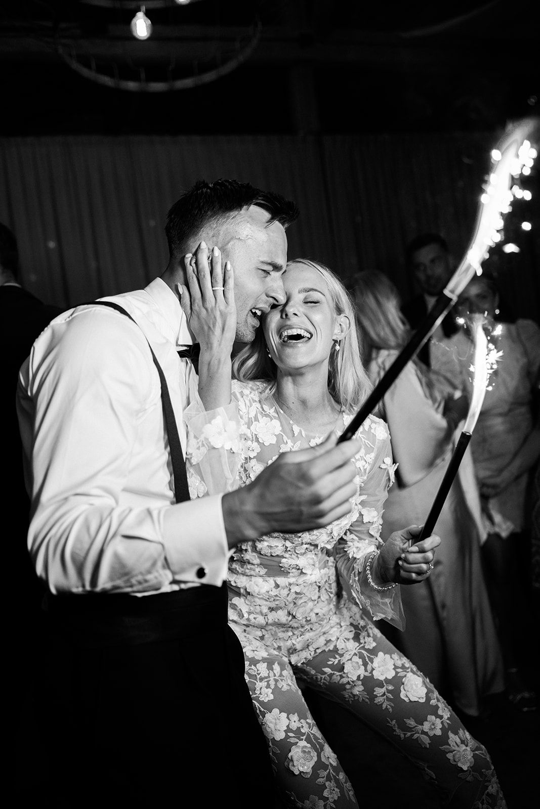A couple shares a joyful moment on the dance floor while holding sparklers at a wedding celebration.