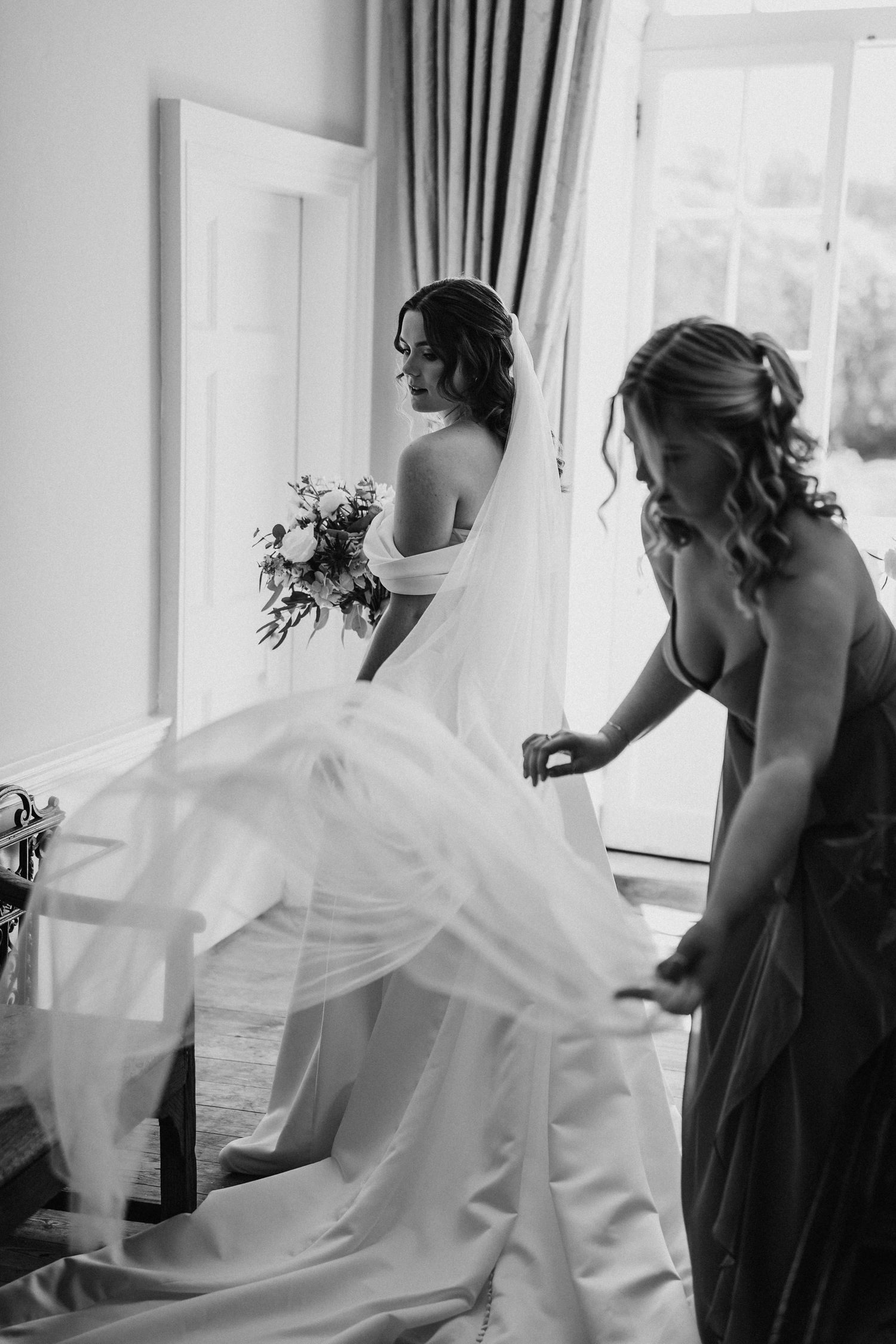A flowing white wedding dress is being prepared near a bright sunny window.