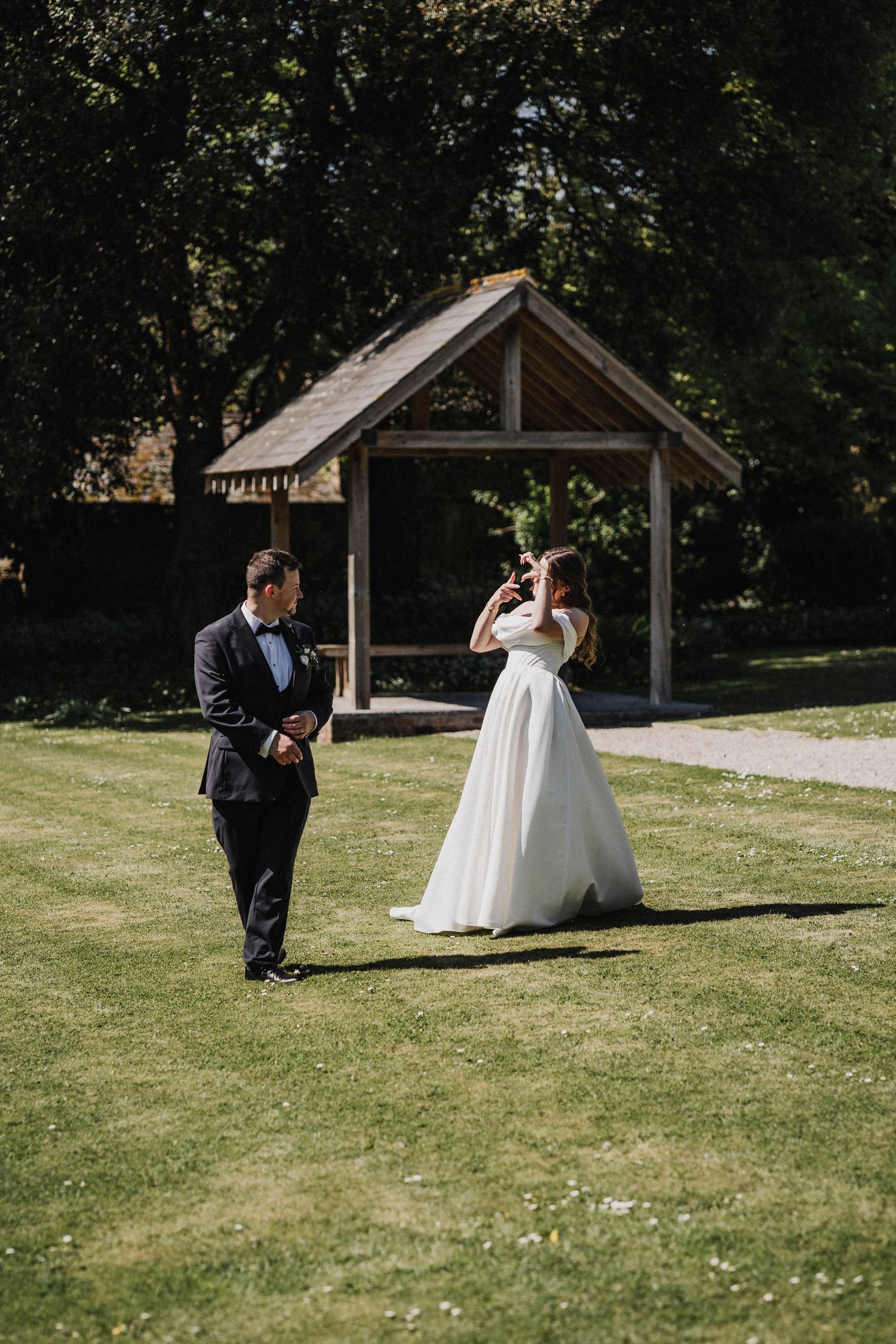 A couple takes romantic wedding photos against a scenic outdoor backdrop with wooden gazebos on a sunny day.