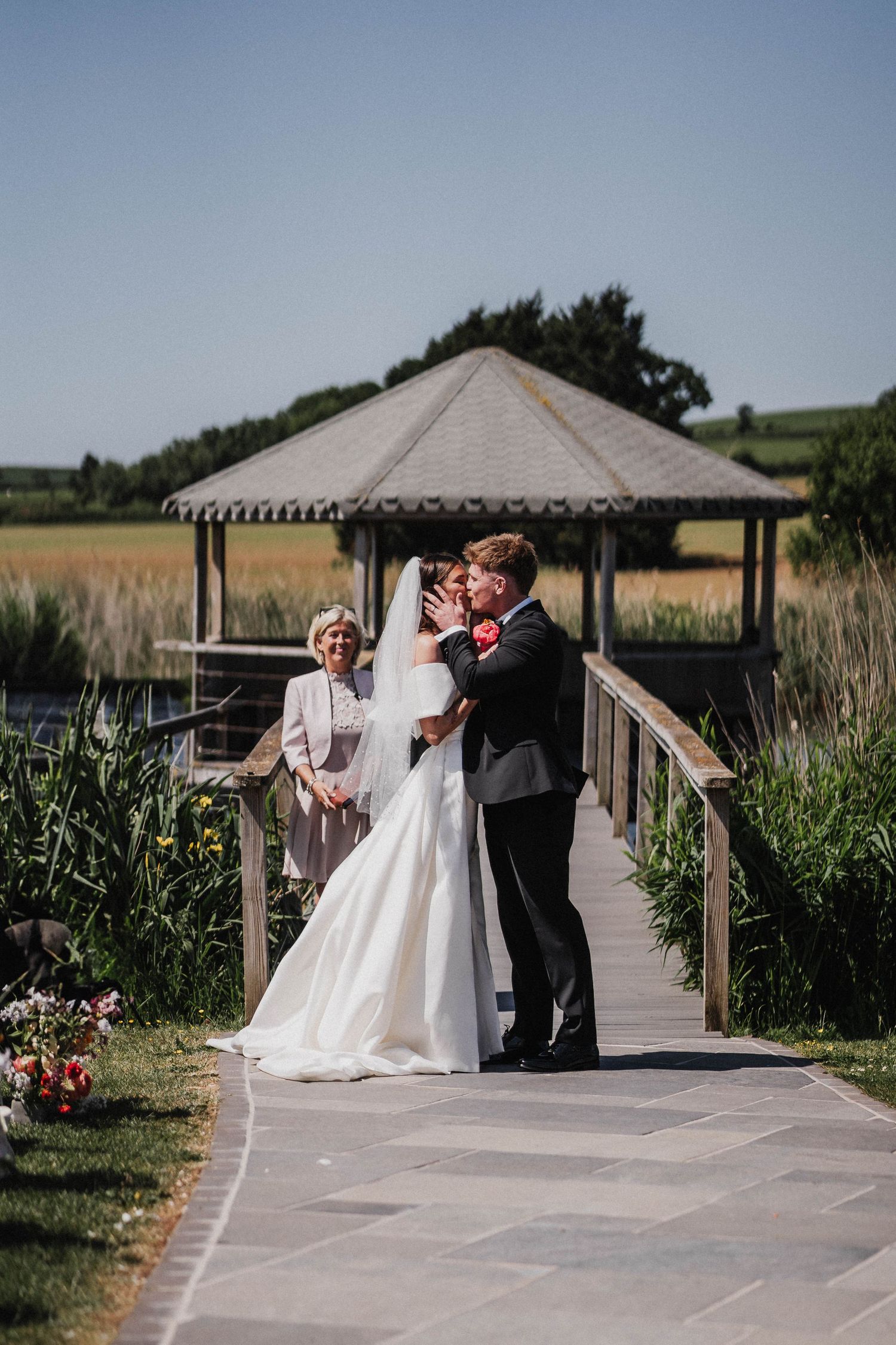 A couple walks along a wooden boardwalk surrounded by tall grass, cattails and golden farmland on their wedding day.