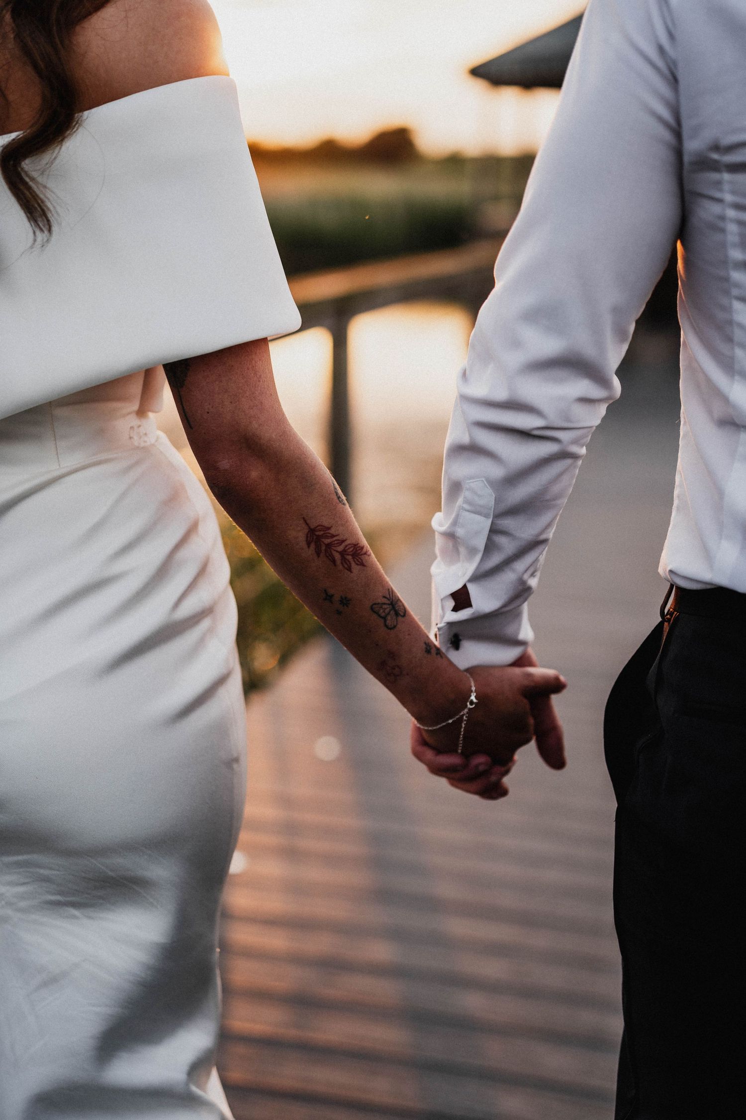 Close-up shots of a bride in a fitted white dress and groom in formal wear holding hands on a dock.