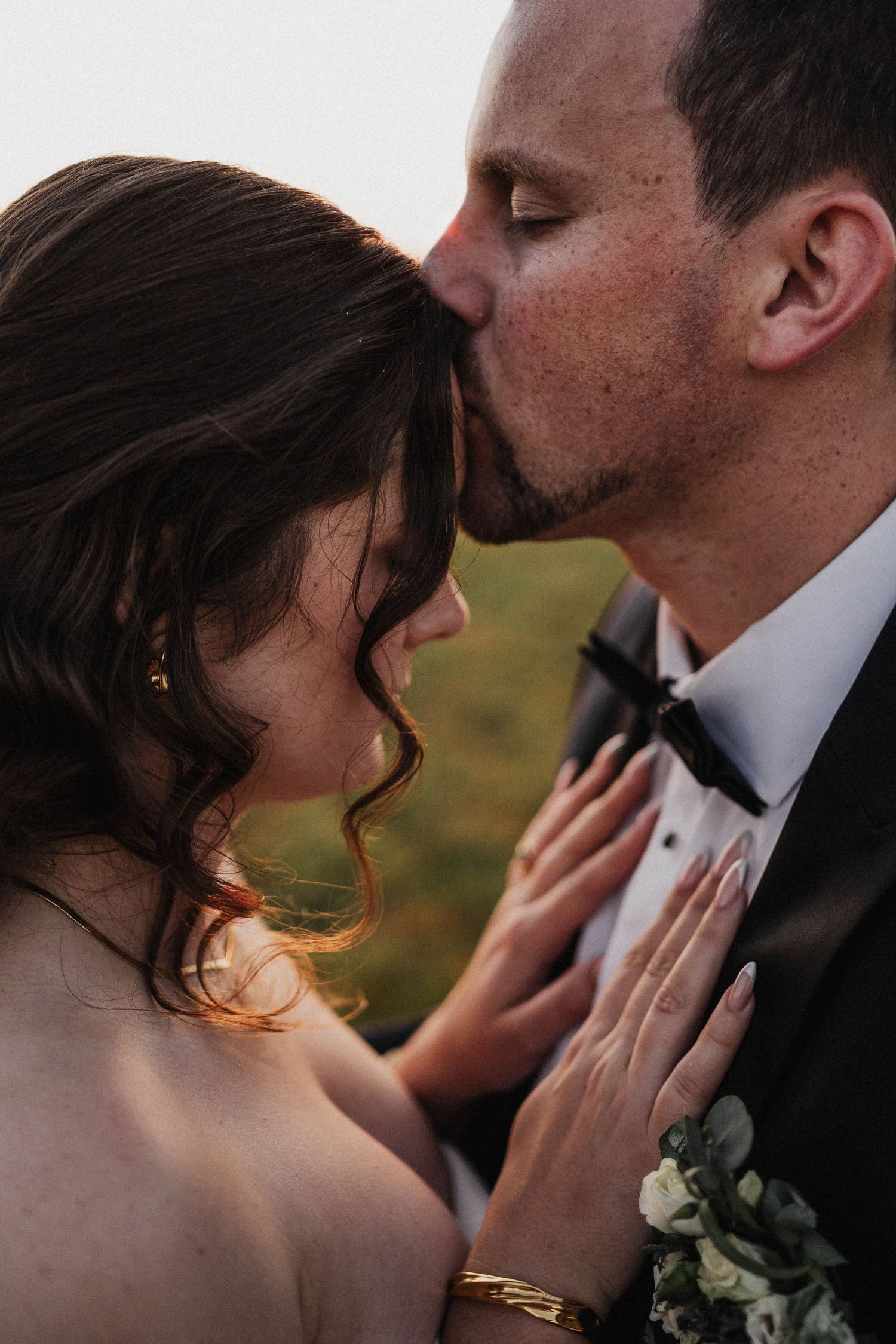 Couple in wedding attire share an intimate kiss as her hand gently rests on his face at sunset.