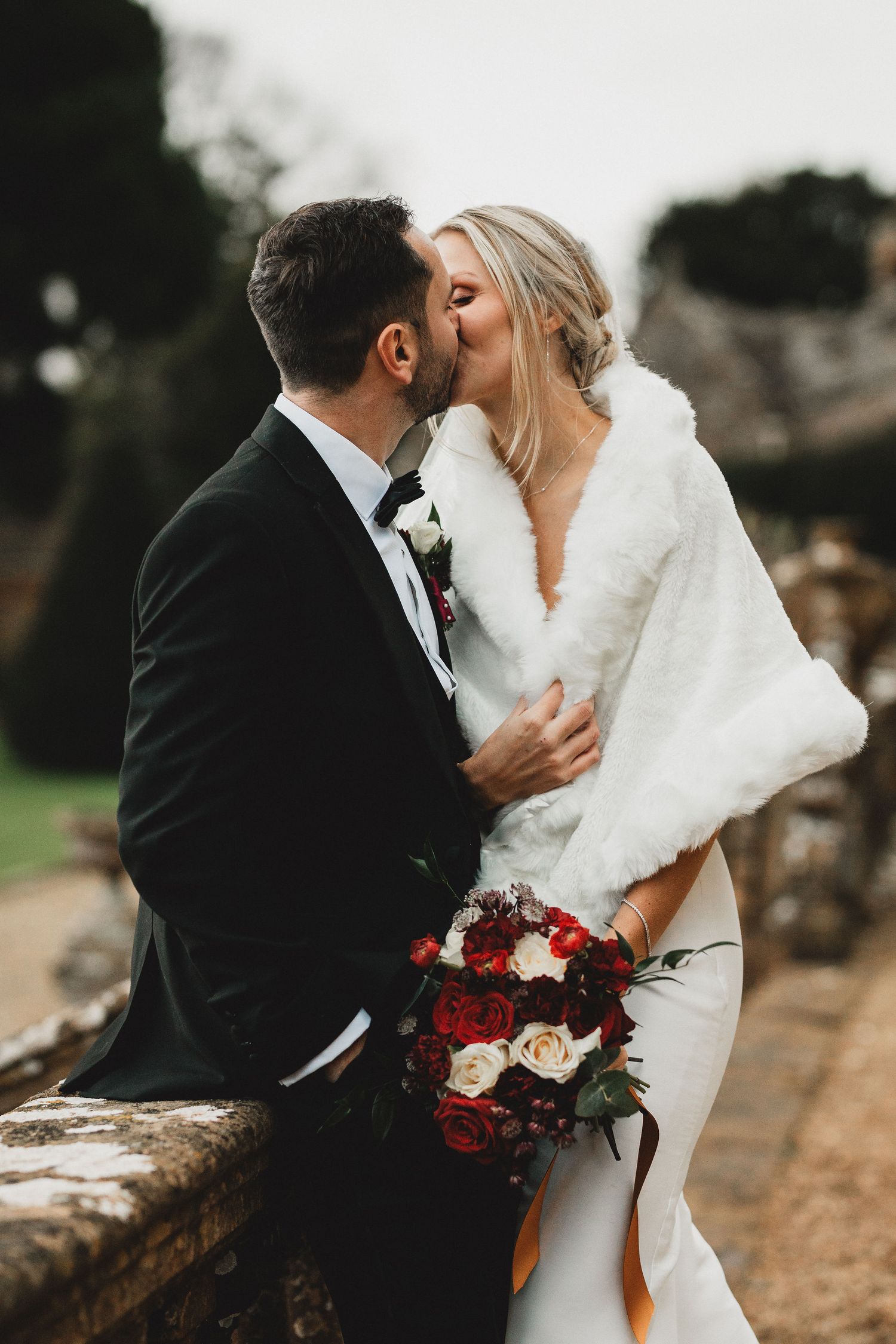 A romantic winter wedding couple shares intimate kisses in a series of outdoor photos with red and white bouquet details.