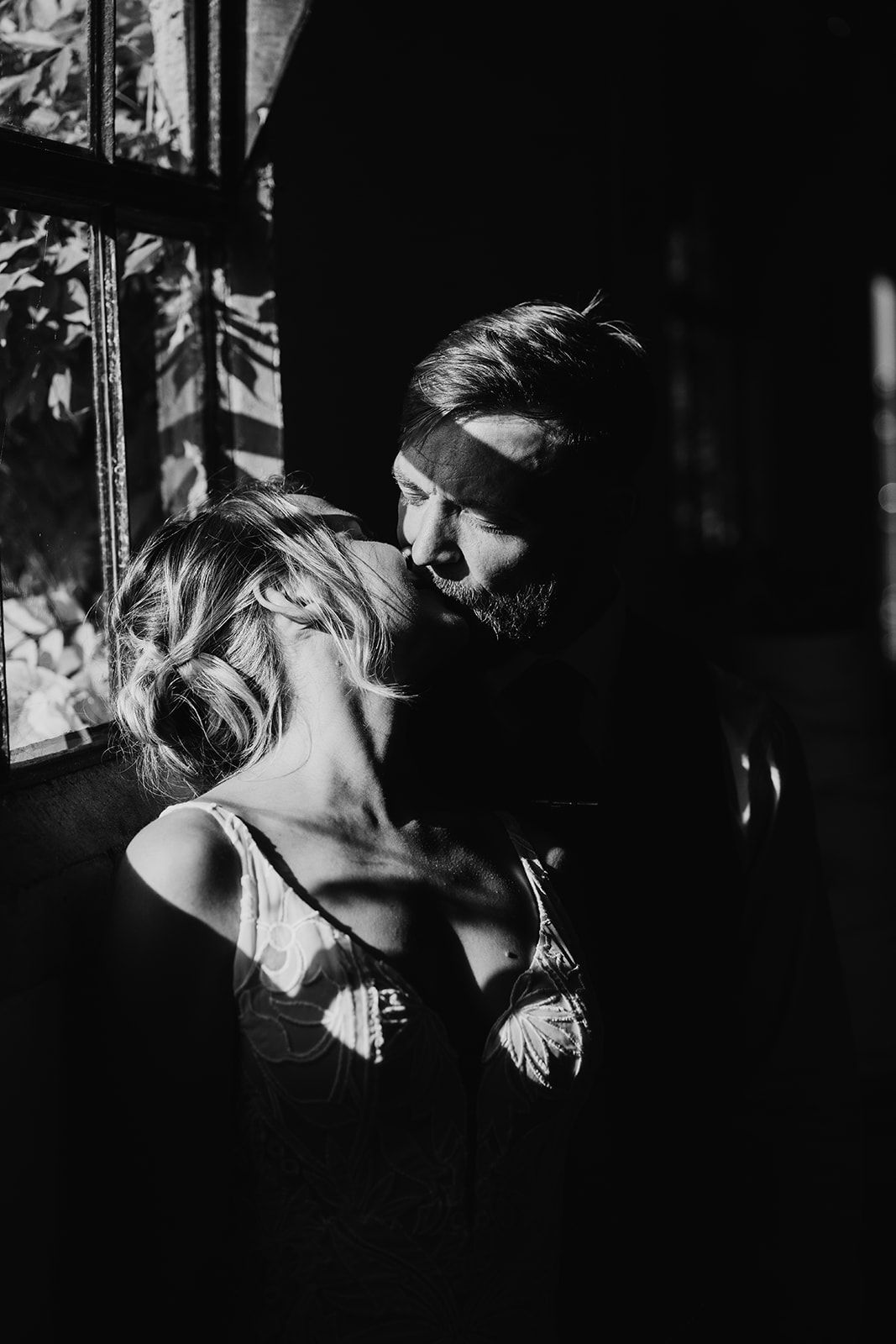 A dramatic black and white intimate portrait capturing light and shadow through window blinds.