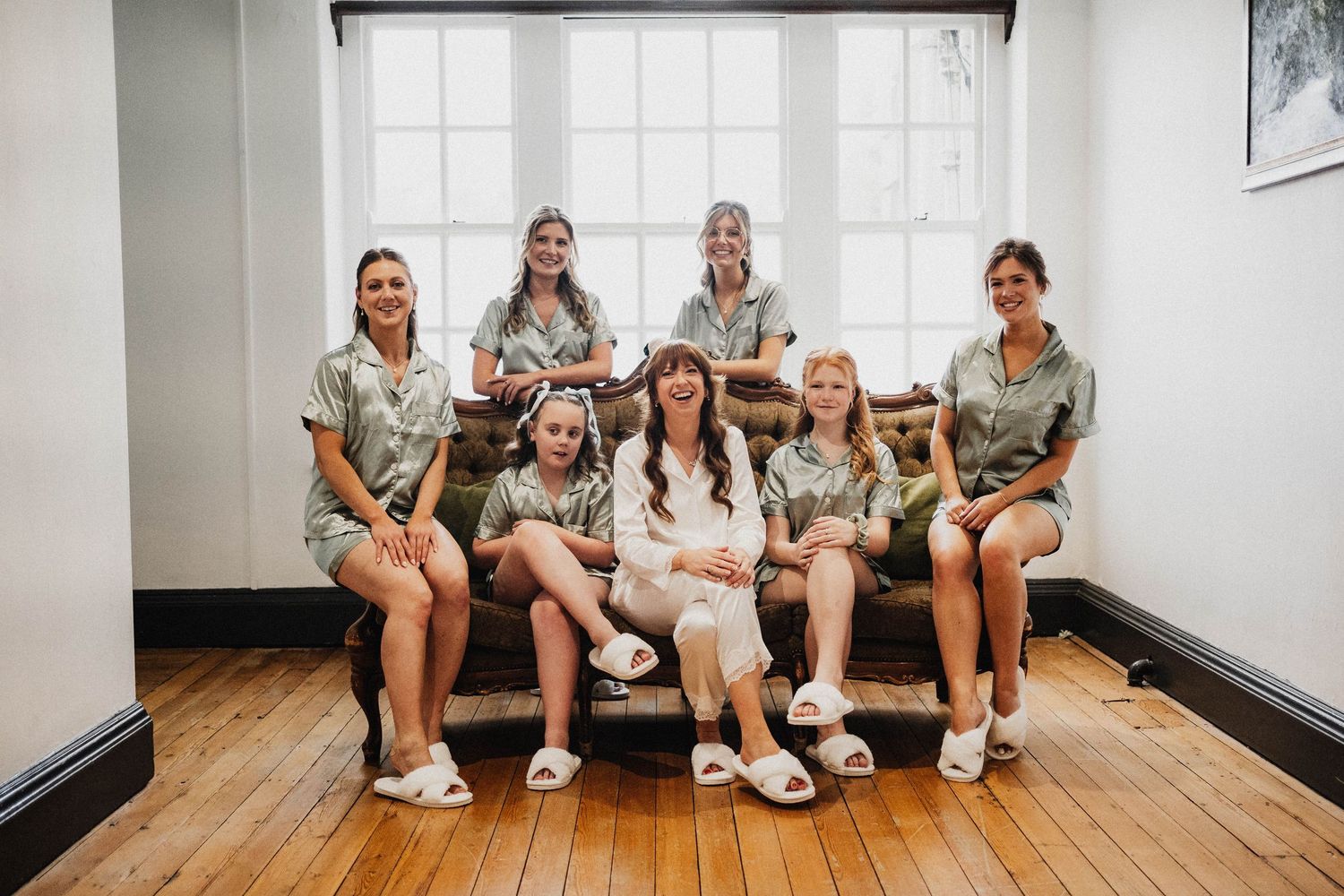 Group wearing matching sage green outfits and white shoes sits together on a couch in a bright indoor setting.