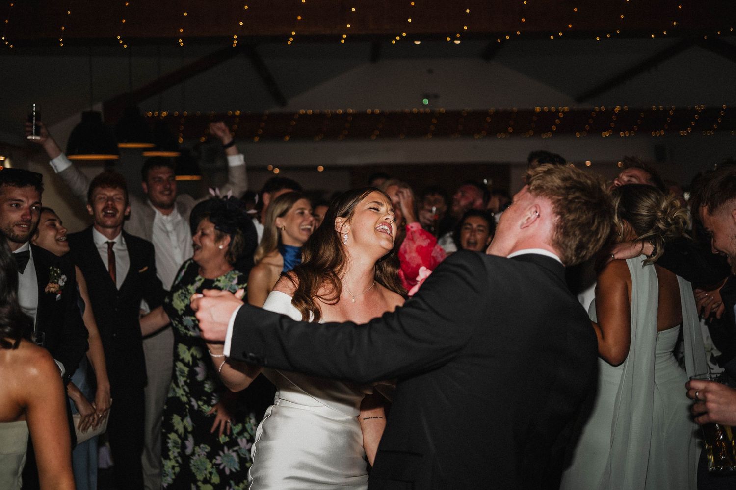 A couple share a joyful moment dancing together at their wedding reception while guests watch and celebrate in the background.