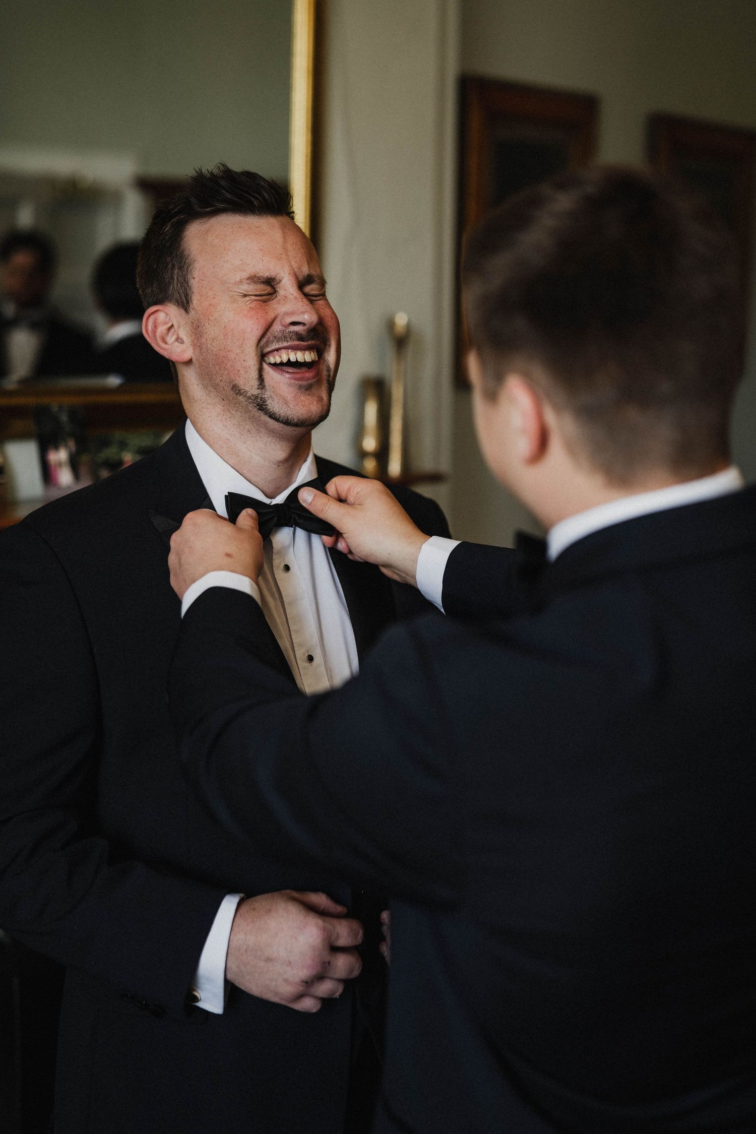 Groomsmen sharing laughs and embracing in a candid moment during formal wedding preparations.