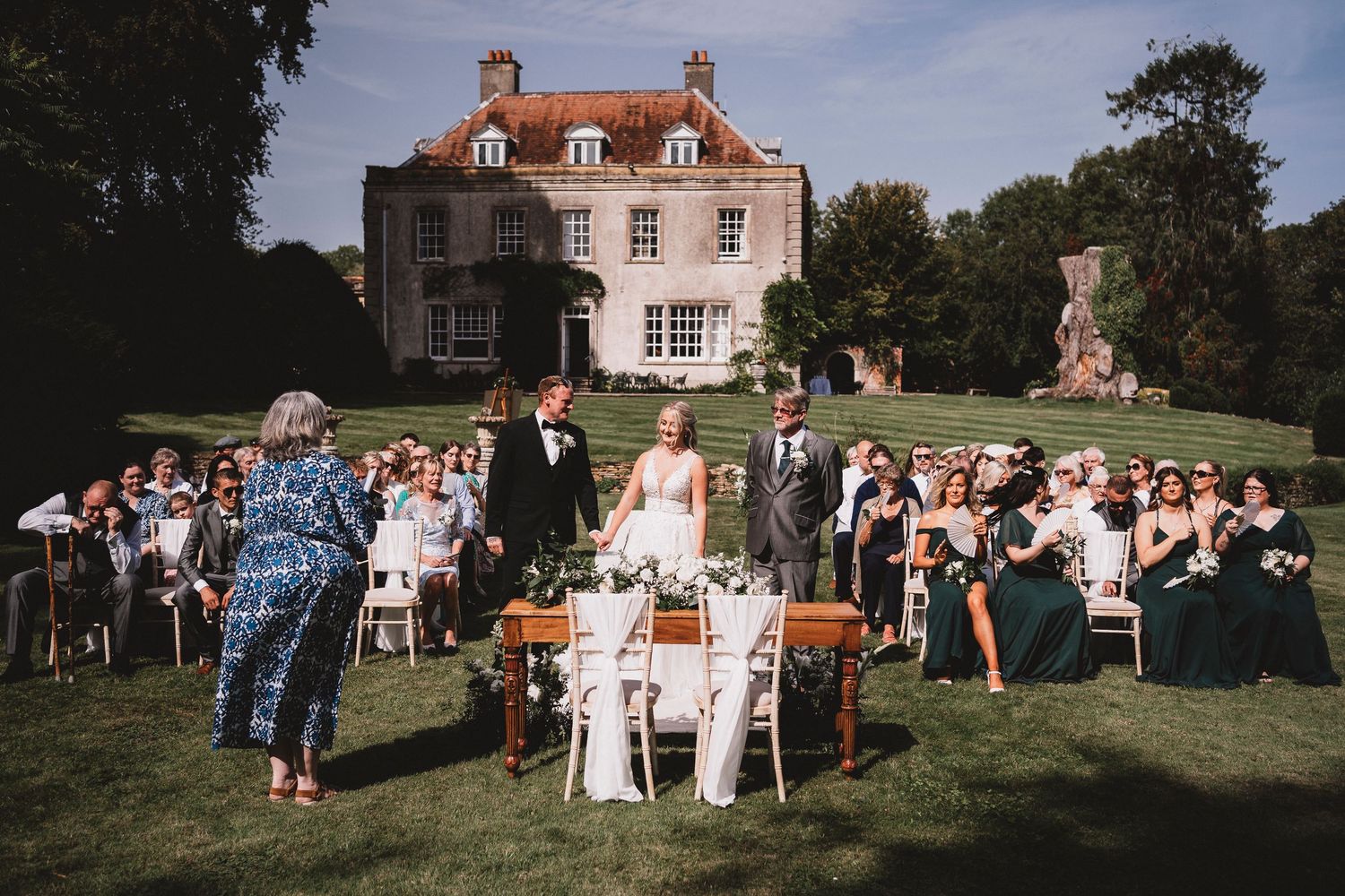 Wedding guests enjoy outdoor garden party celebration at sunset on the lawn of an elegant English country estate.