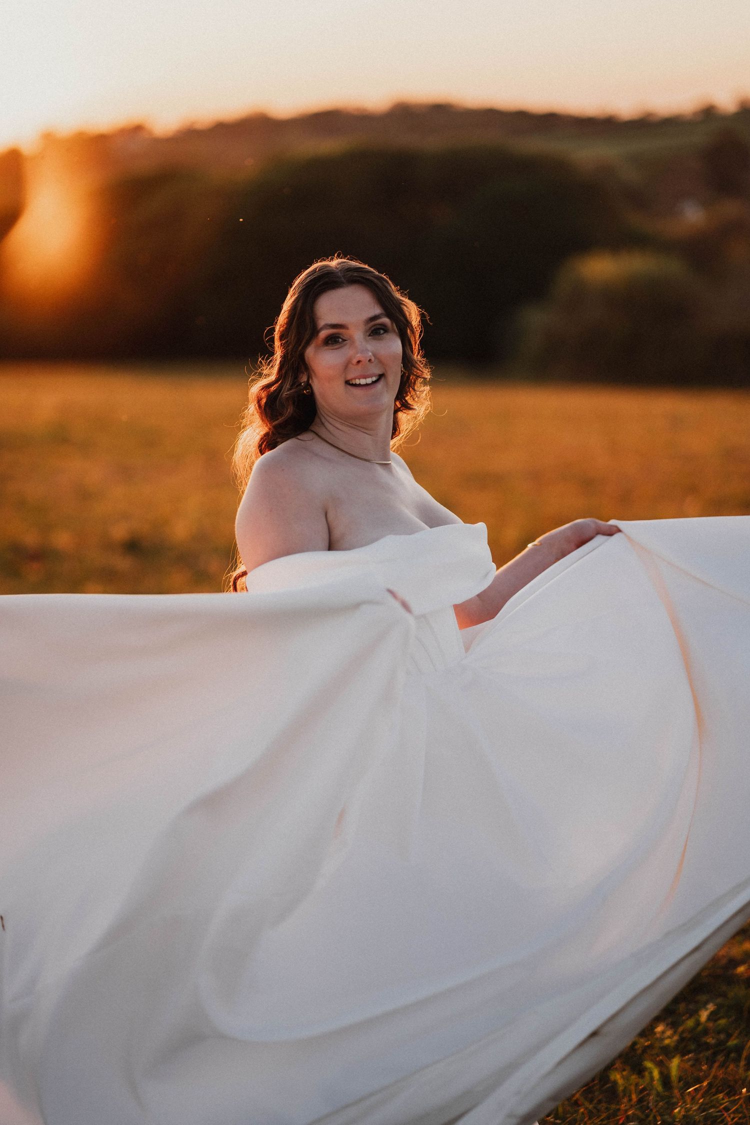 A person in a white wedding dress twirls in a golden sunset field creating a dreamy romantic atmosphere.