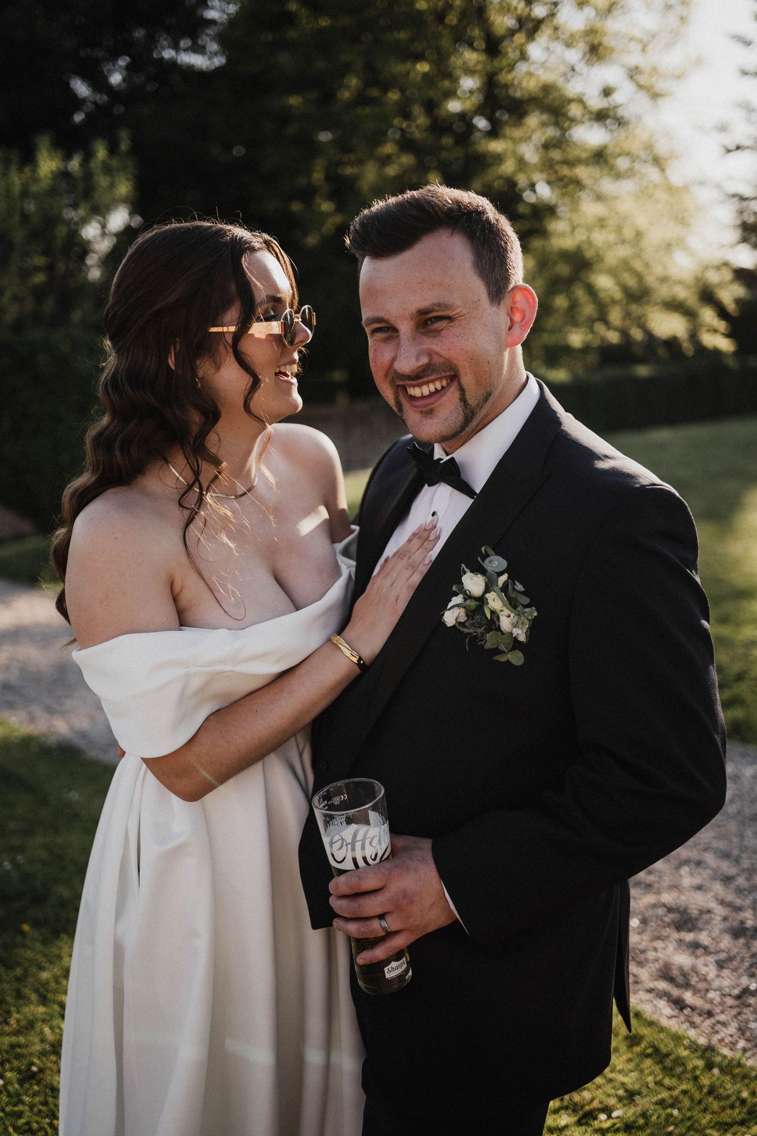 A couple in wedding attire shares intimate moments outdoors during golden hour with champagne glasses in hand.