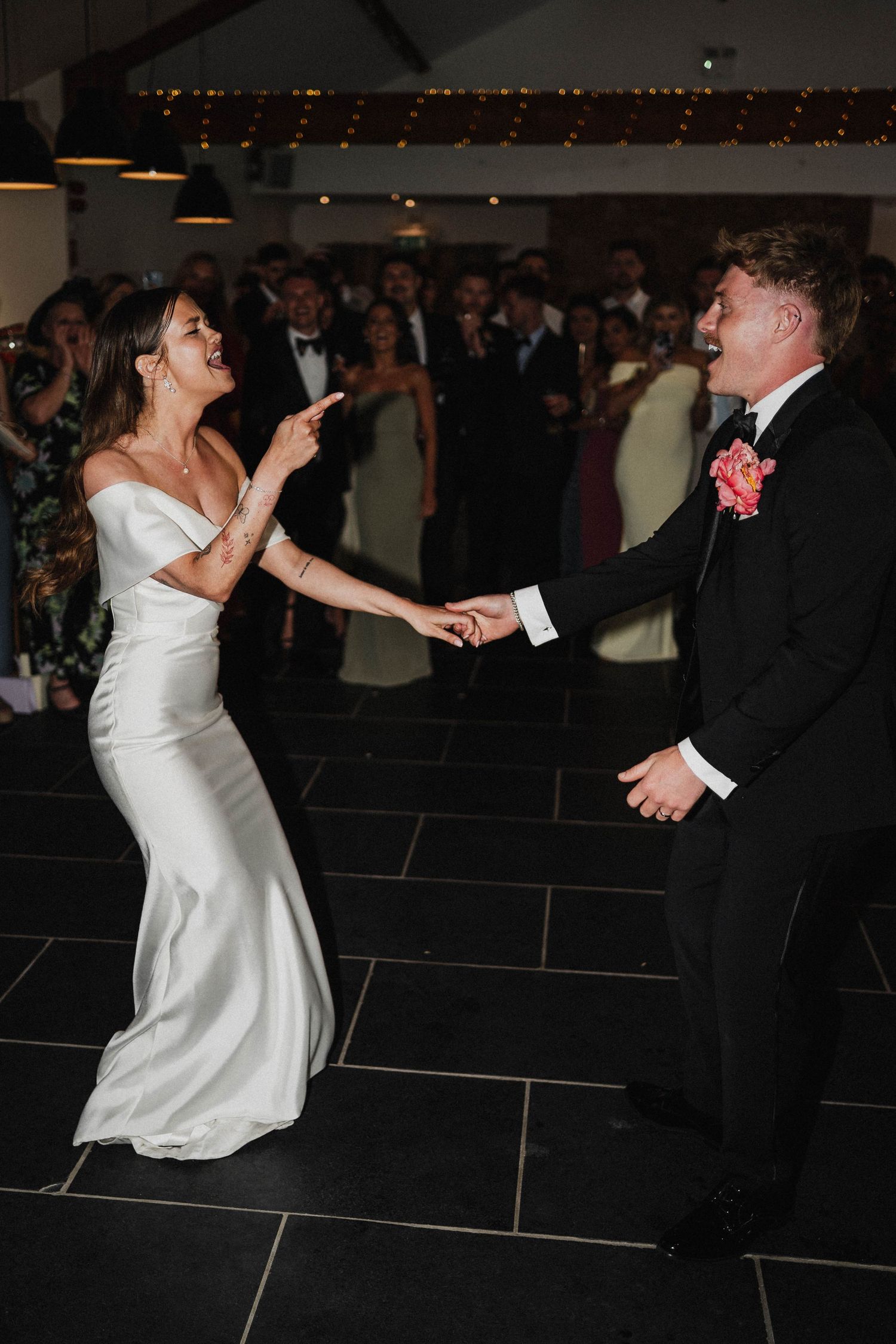 Newlyweds share a joyful dance moment on their wedding day as they move across a dark tile floor in formal attire.