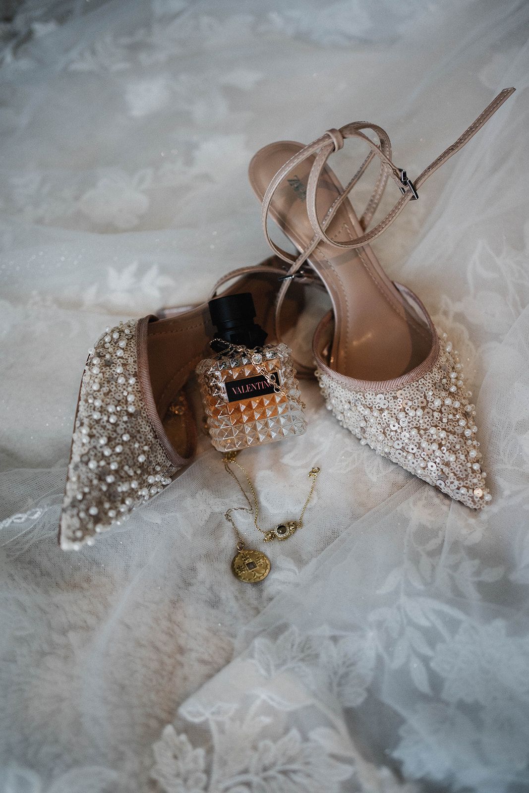 Elegant jeweled nude wedding heels with pearl embellishments resting on white tulle fabric creating a romantic bridal setting.