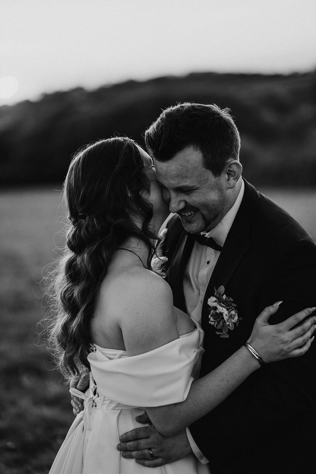 Black and white intimate wedding photo showing a tender moment between a bride in white dress and a groom in tuxedo.
