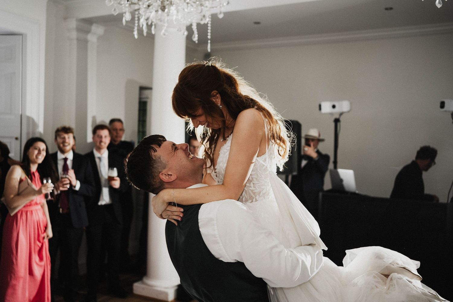 A romantic moment is captured at an elegant wedding reception under a crystal chandelier as the couple embrace and dance.