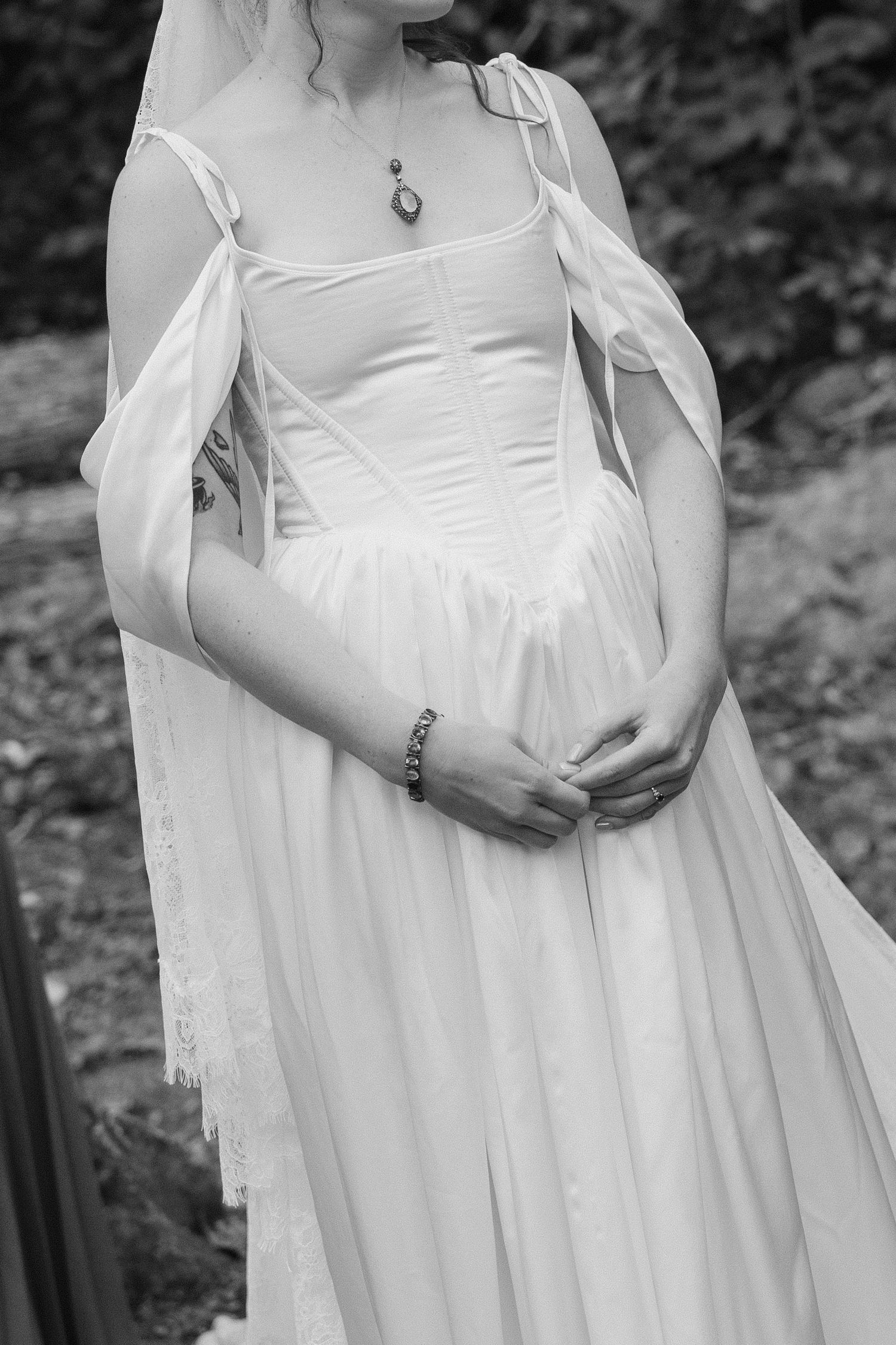 A figure in a flowing white vintage dress with delicate sheer sleeves stands in a natural outdoor setting.