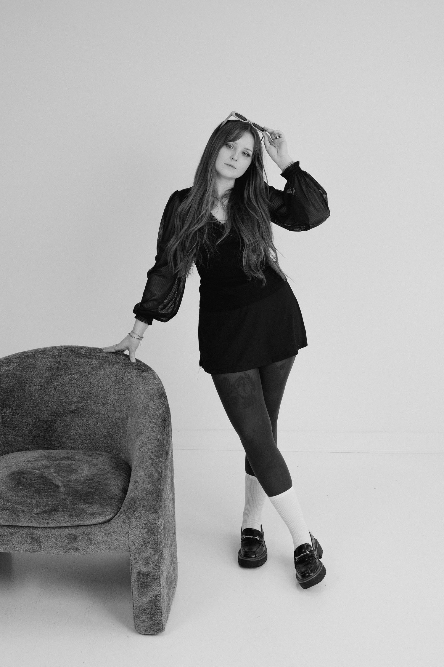 Black and white artistic photo series showing a figure in dark clothing posed with a minimalist sofa against white backdrop.