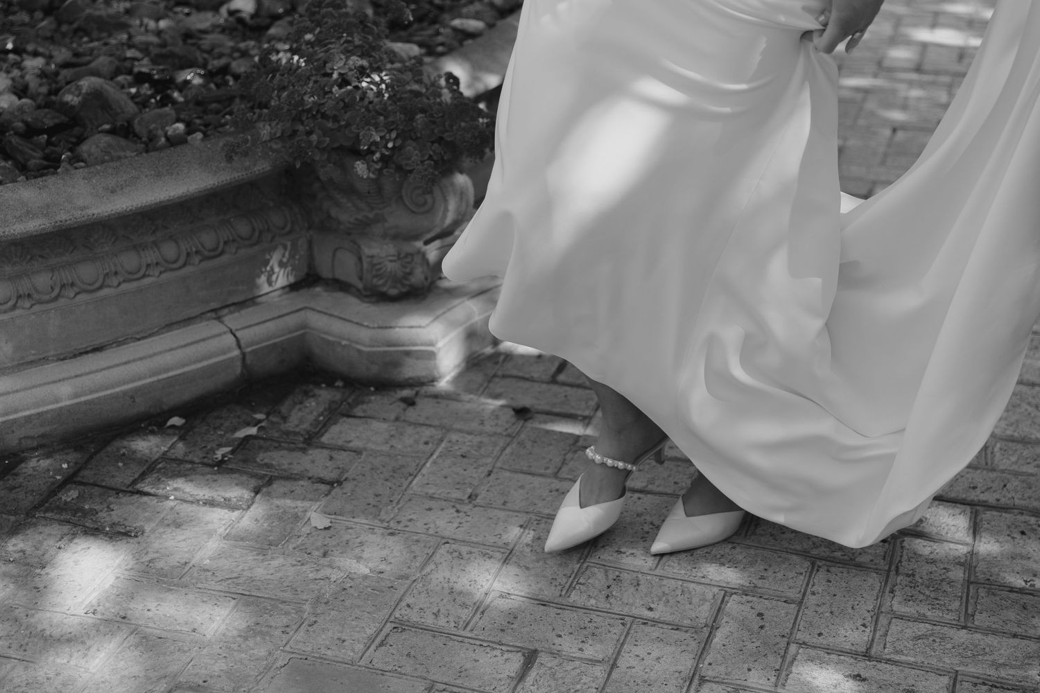 Close up of a wedding dress hem and shoes on brick pavement with dappled sunlight, in Greensboro, NC.