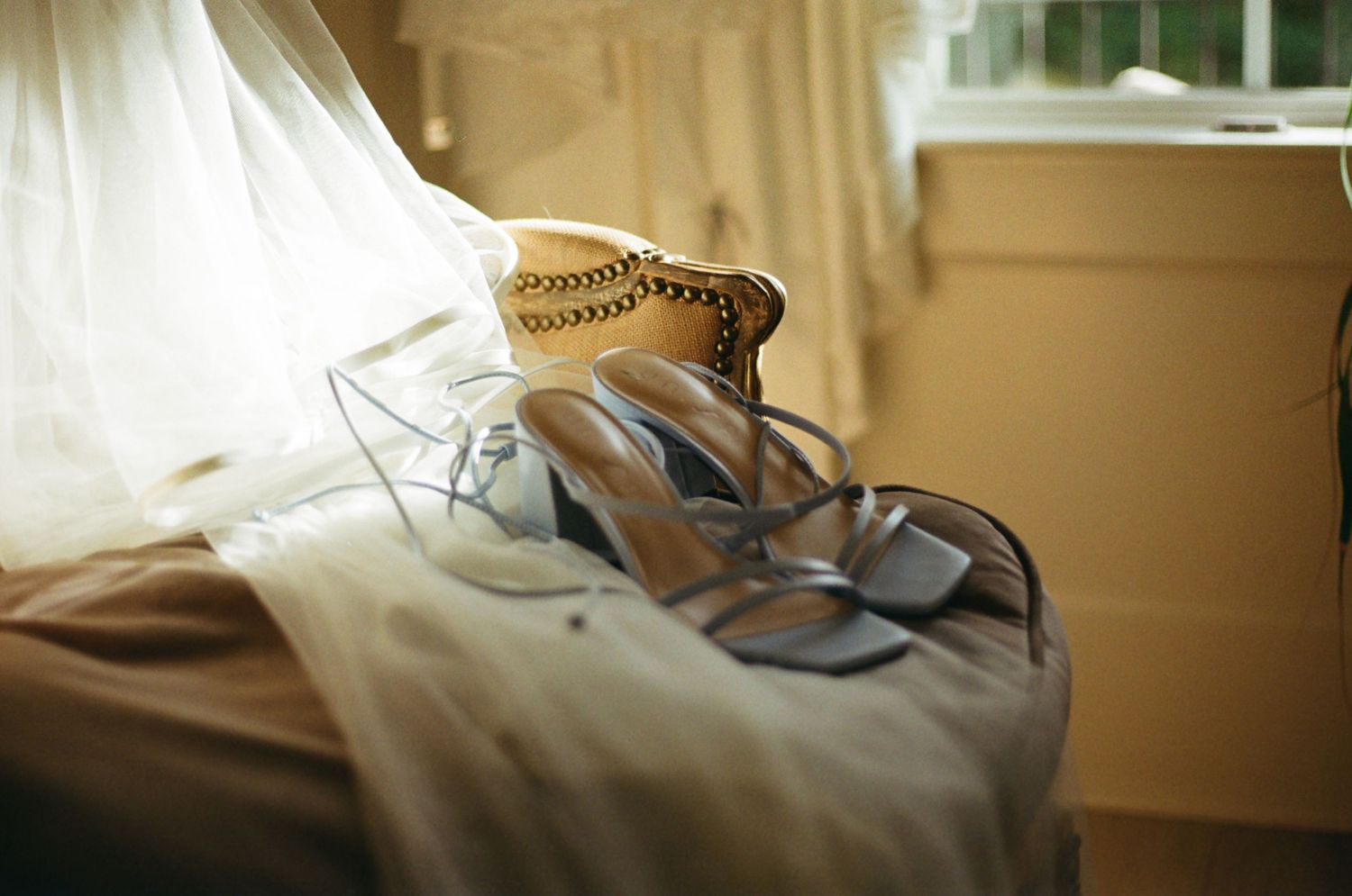 A pair of silver heels and bridal accessories rest on cream-colored fabric in soft window light.