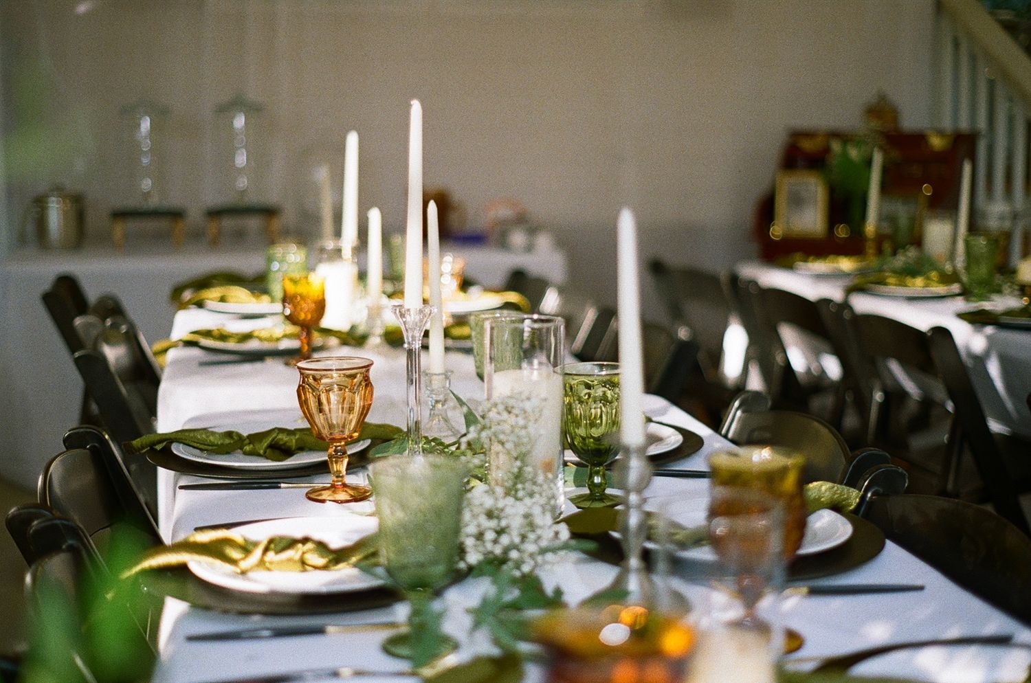 Elegant dinner table setting with tall white candles, crystal glasses and formal place settings in warm lighting on film in Waxhaw NC