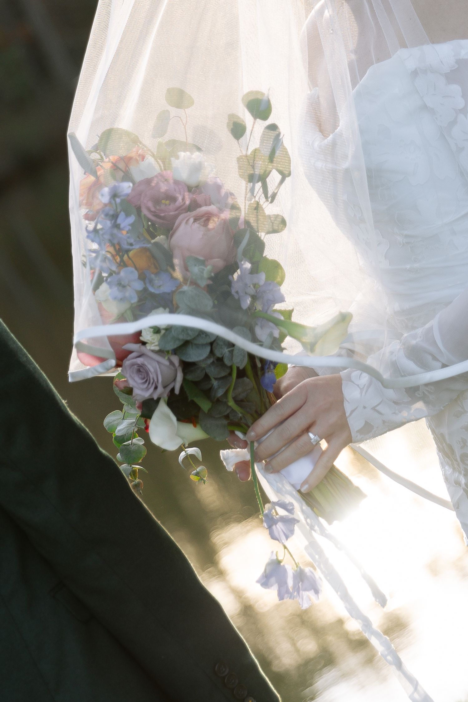 Sunlit wedding bouquet with pastel flowers and greenery seen through sheer white veil in Raleigh, NC.