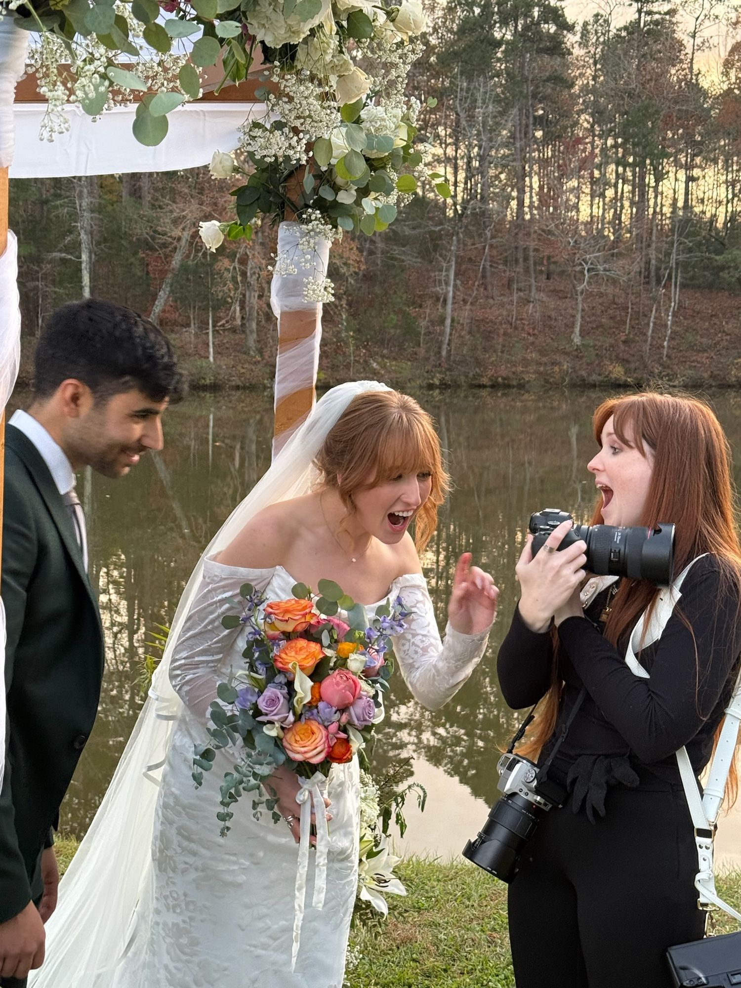 A joyful outdoor wedding moment in Durham, NC captured near a lake at sunset with white floral decorations and a vibrant bridal bouquet.